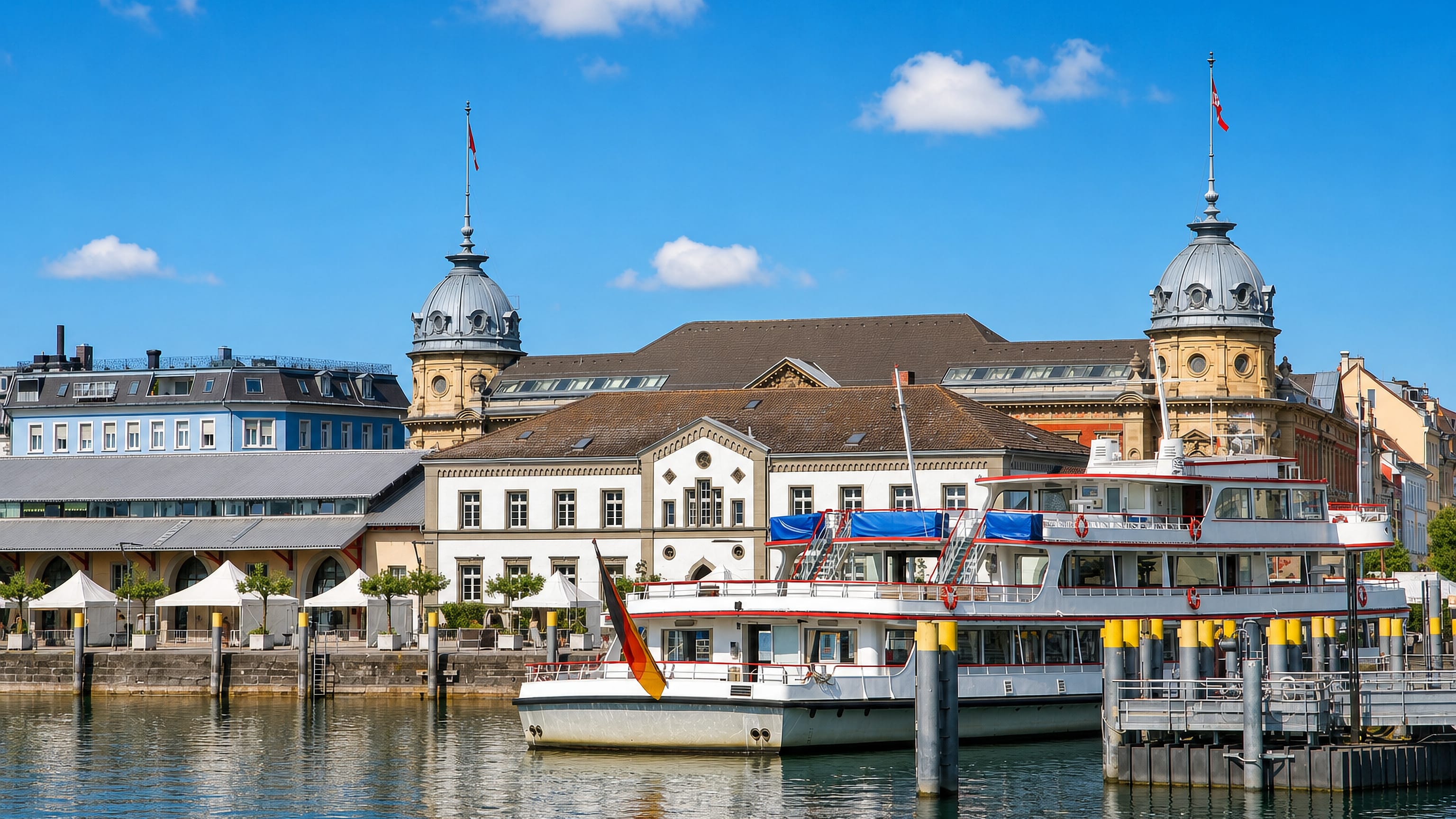 Konstanz harbour on Lake Constance with a moored passenger ferry and the domed towers of the historic station.