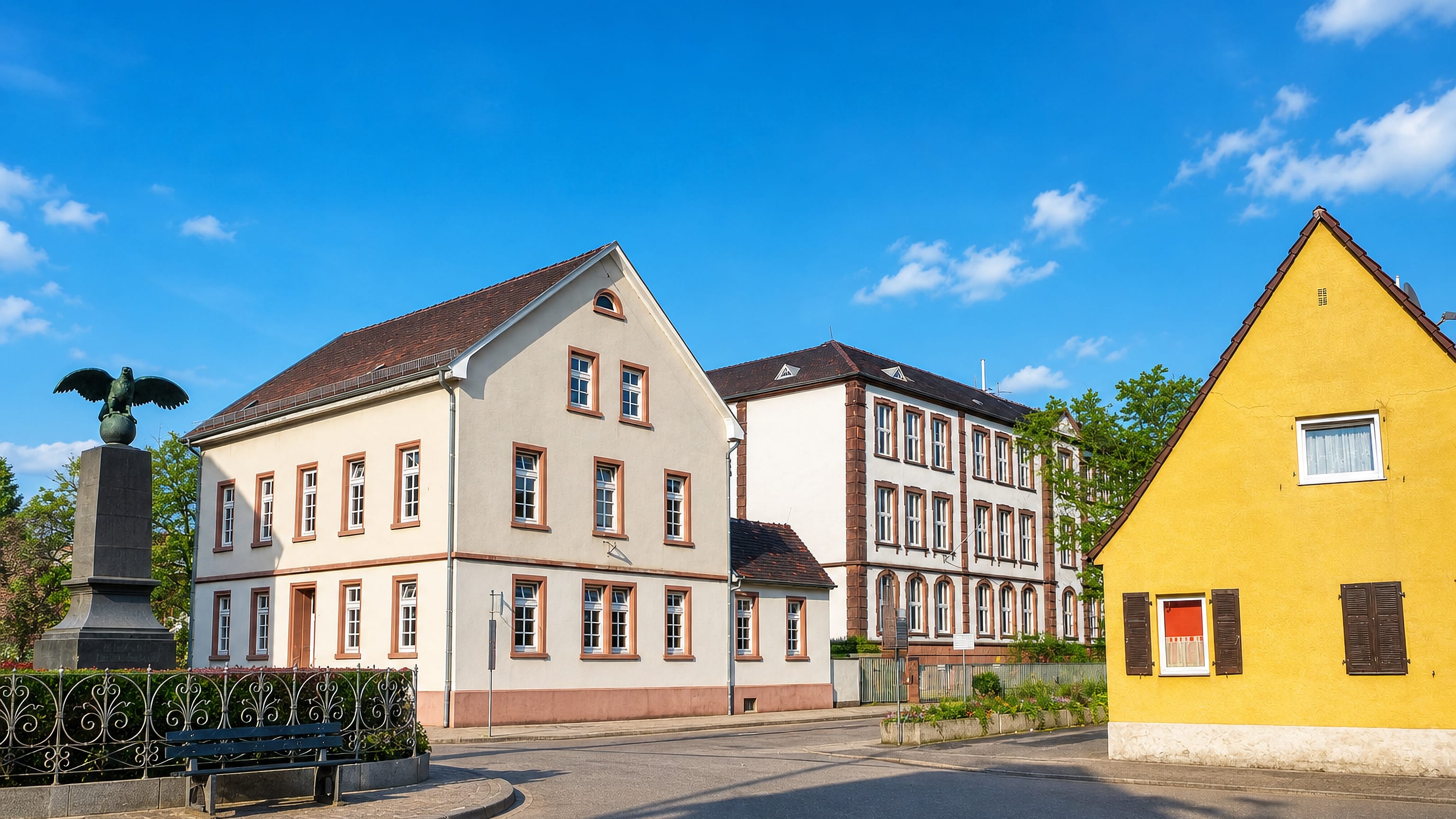Village centre of Sandhofen in Mannheim, with an eagle war memorial, old school building and yellow gabled house.