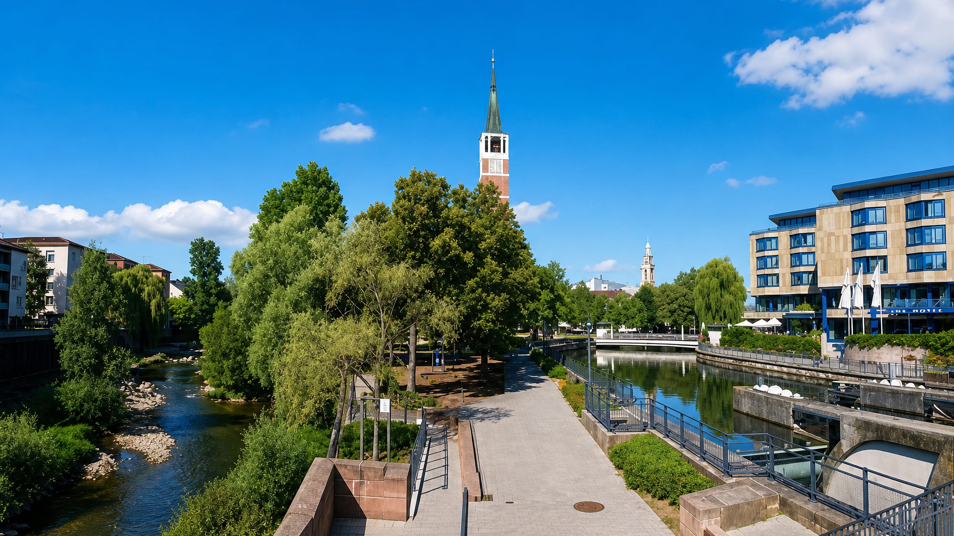 Riverside promenade along the Enz in Pforzheim, with a green-spired church tower and a modern hotel across the water.