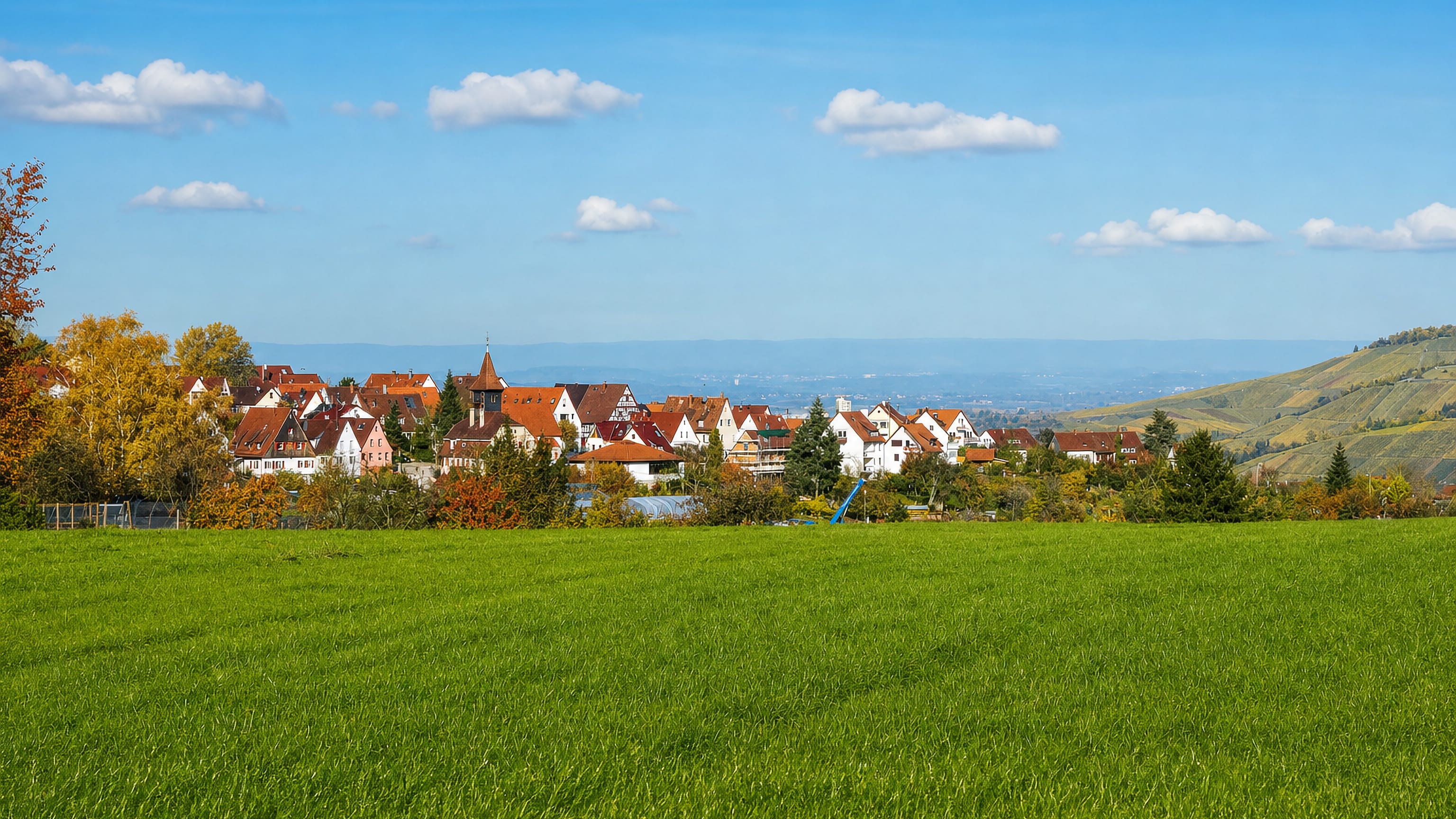 Red-roofed houses and a church tower on the hillside above green meadows in Heumaden, Stuttgart.