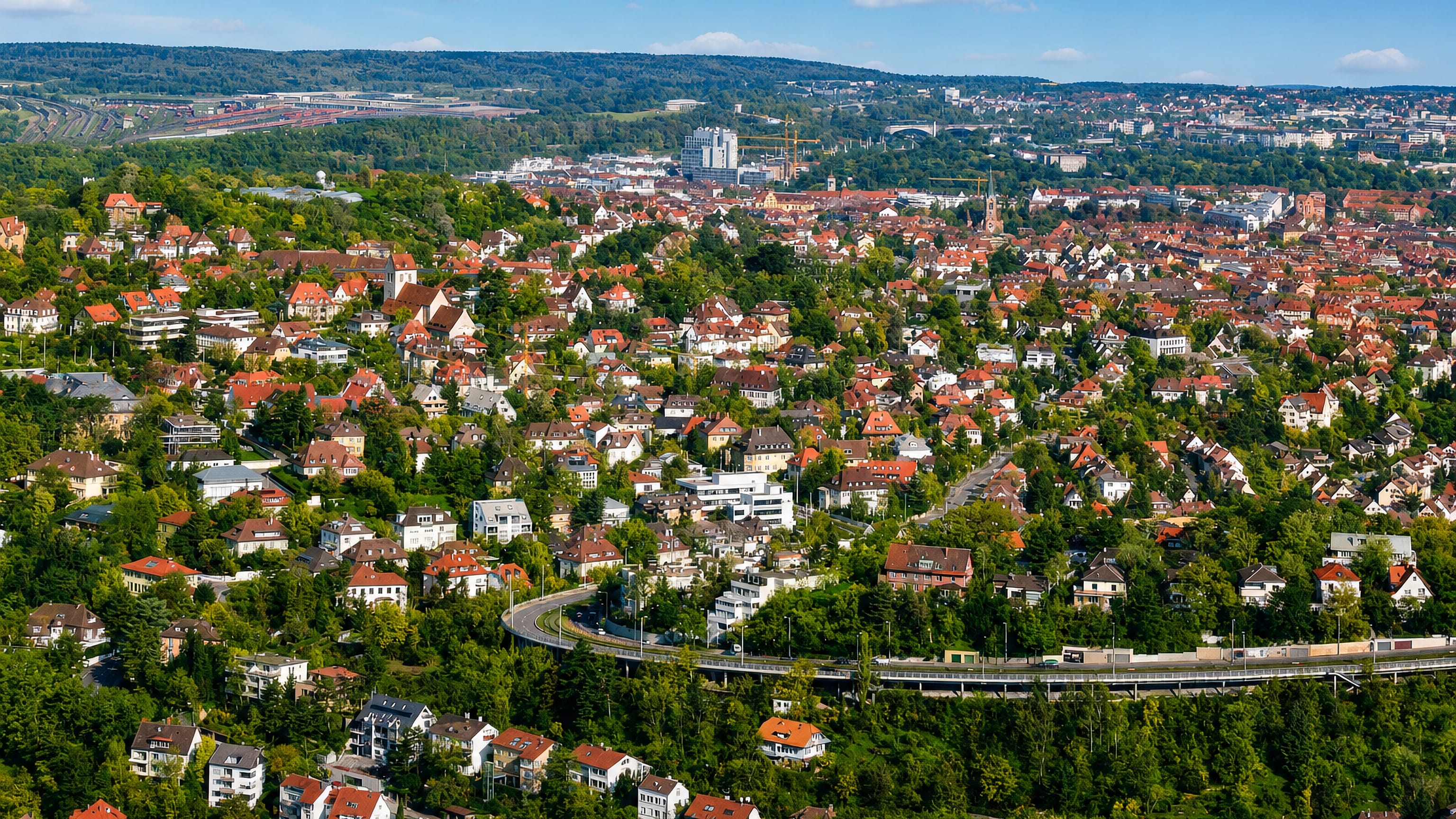 Red-roofed hillside houses of Stuttgart-Ost above a curving road, with the city and wooded hills beyond.
