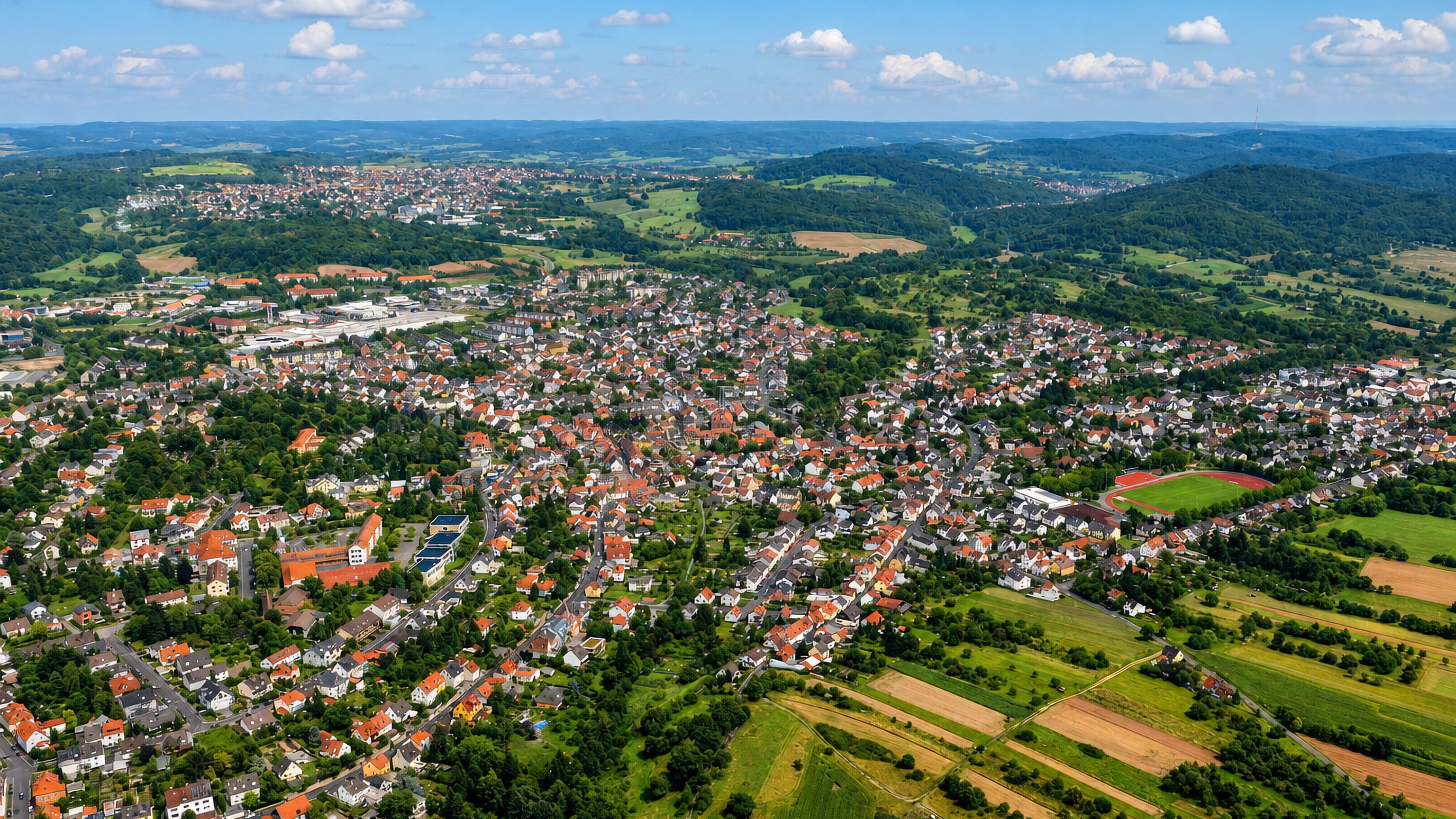 Aerial view over Schweinheim's red-roofed houses on the wooded Spessart edge above Aschaffenburg, Bavaria.