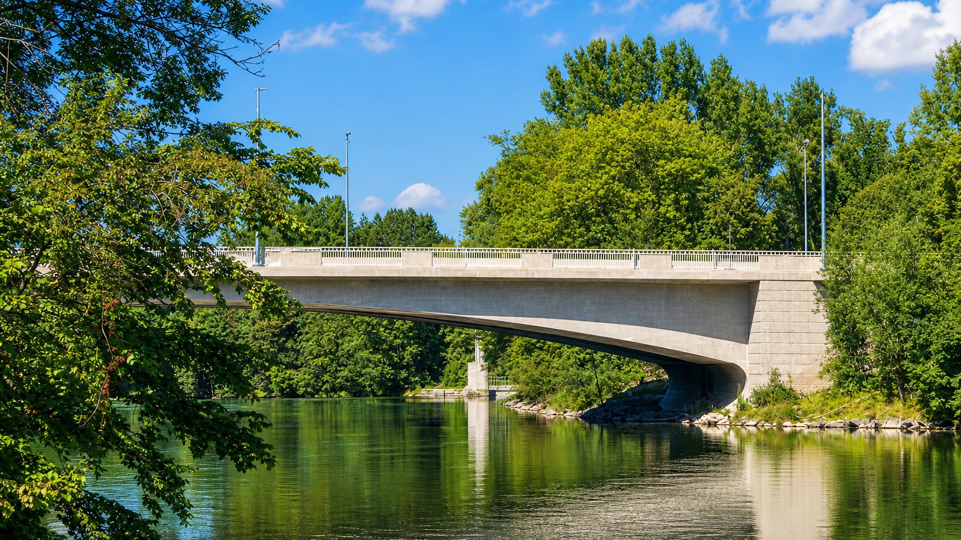 Concrete road bridge over a tree-lined river at Hochzoll in Augsburg on a clear summer day.