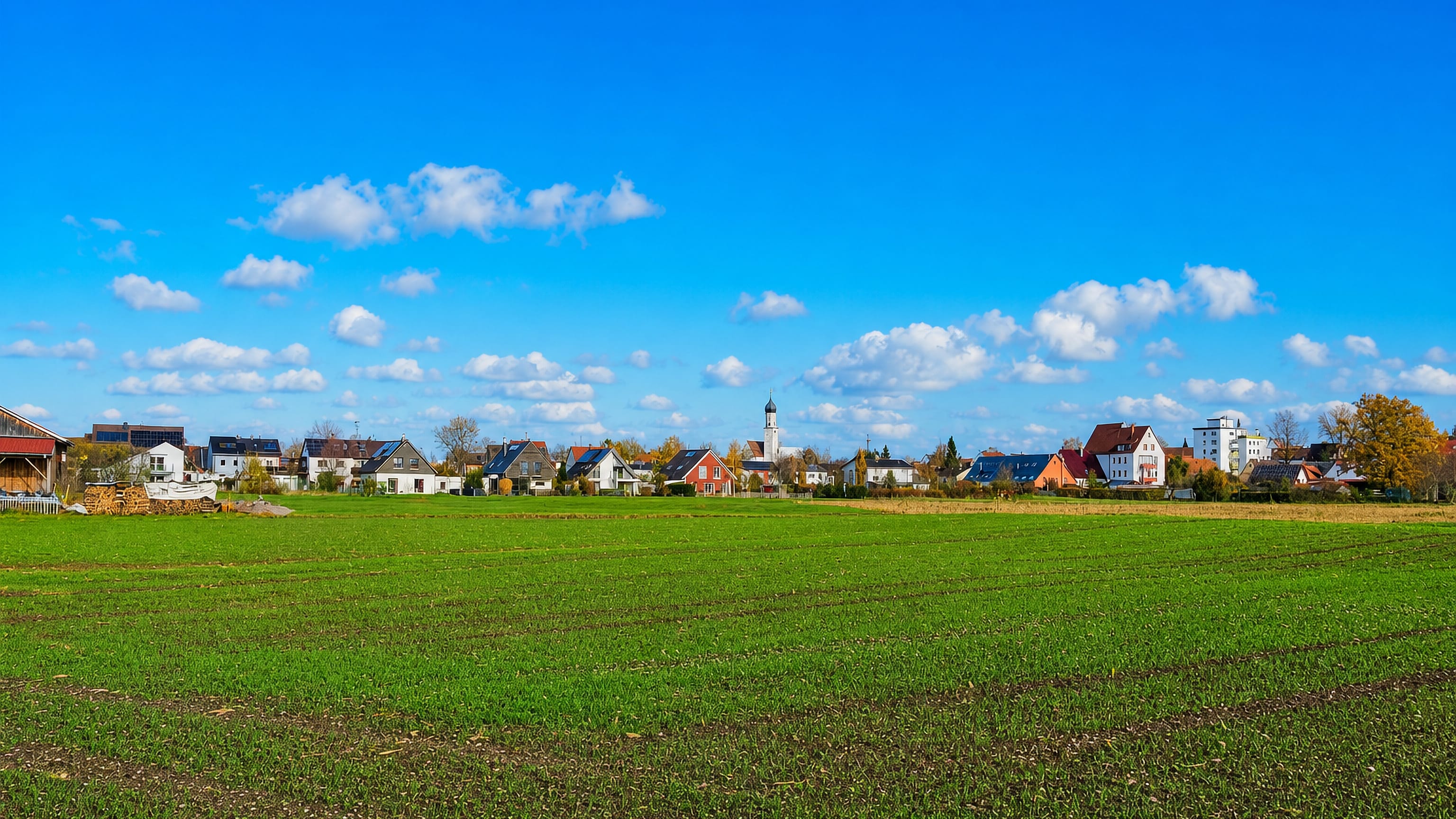 Fields on the edge of Inningen, Augsburg, with the village's onion-domed church tower above red-roofed houses.