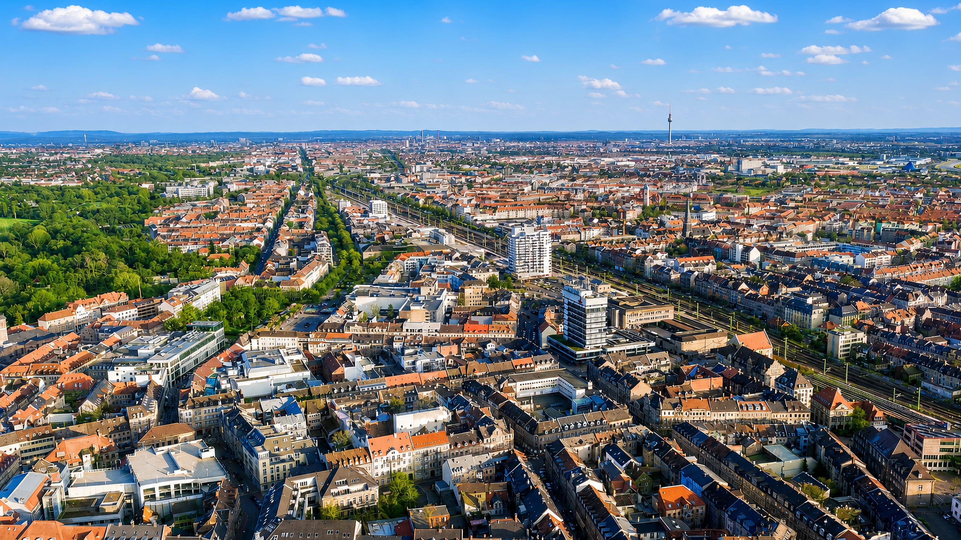Aerial view over Fürth's rooftops and rail corridor, with Nuremberg's television tower on the far horizon