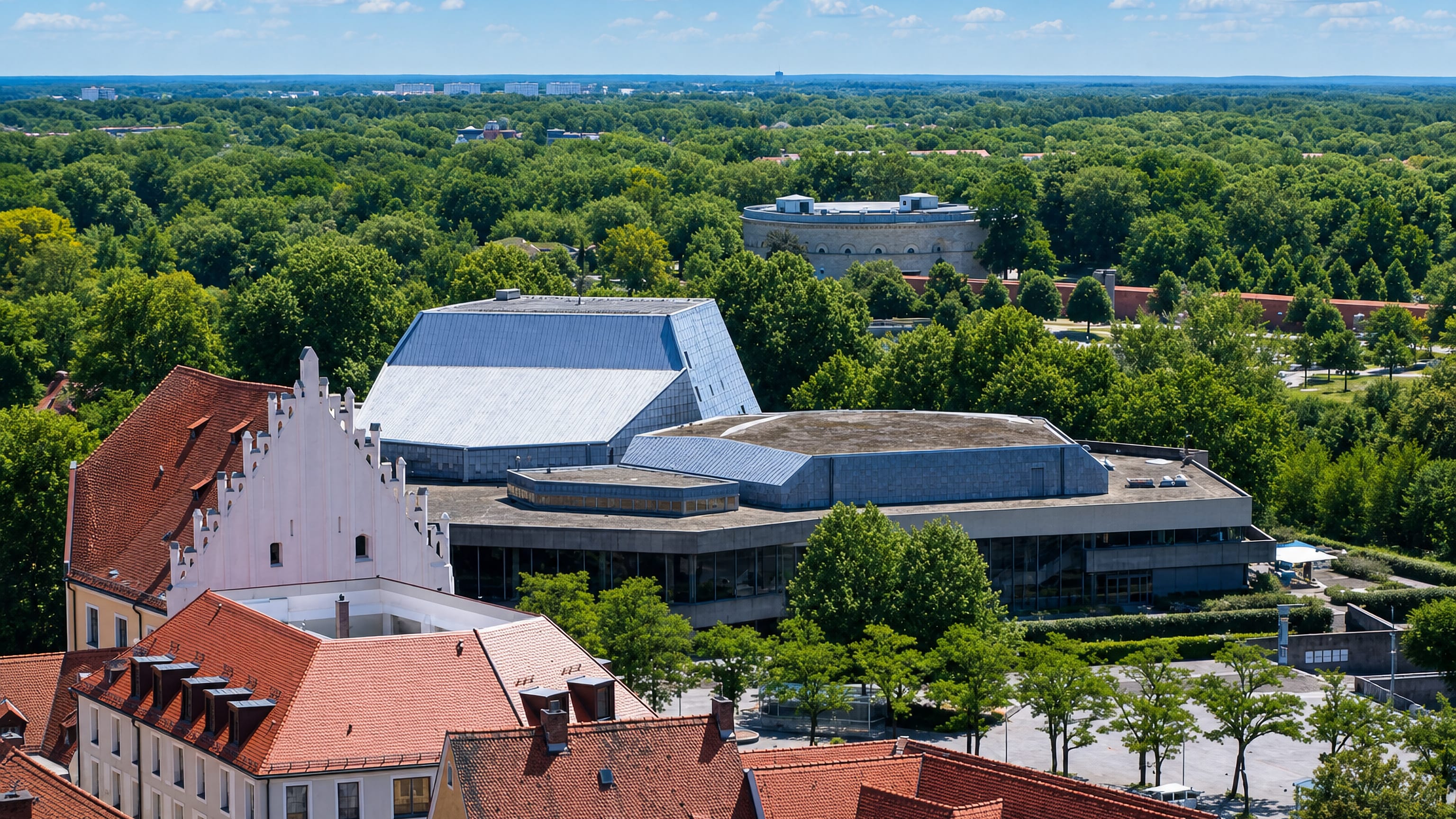 Rooftop view over Ingolstadt with the modernist Stadttheater, a round fortress tower and wooded parkland.