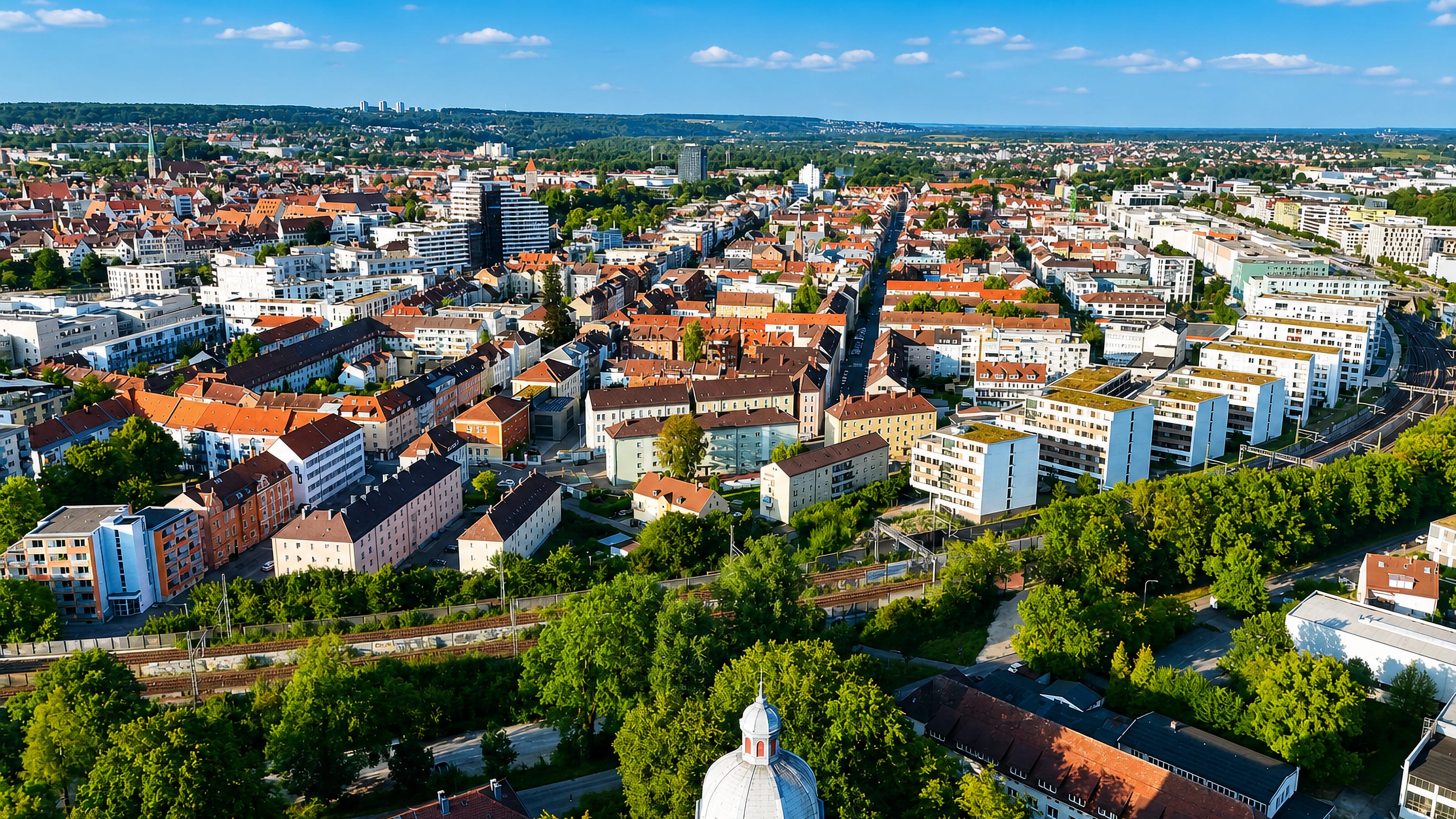 Aerial view over Neu-Ulm, Bavaria, with red-tiled roofs, a domed church tower and rail lines crossing the town.