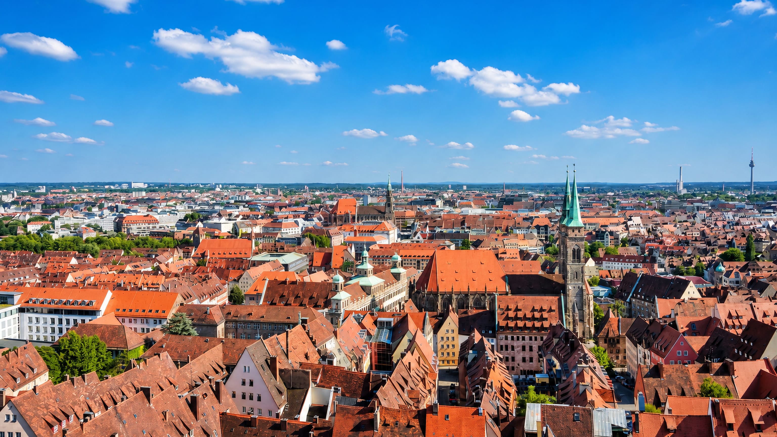 Nuremberg's red-tiled Altstadt rooftops below the twin green spires of St. Sebaldus Church under a blue summer sky
