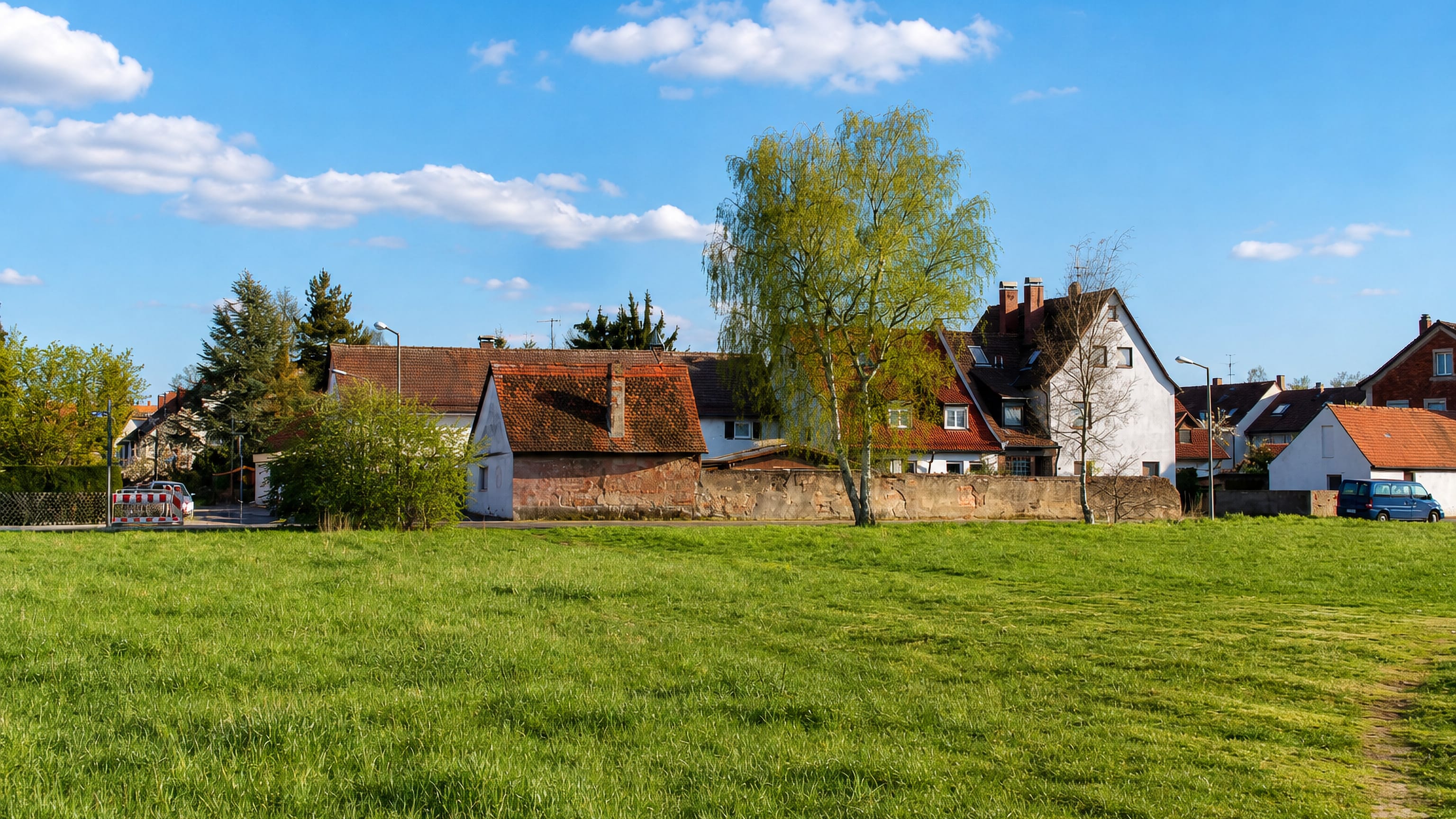 Tiled-roof houses and a sandstone wall behind an open meadow in Ziegelstein, a northern district of Nuremberg.