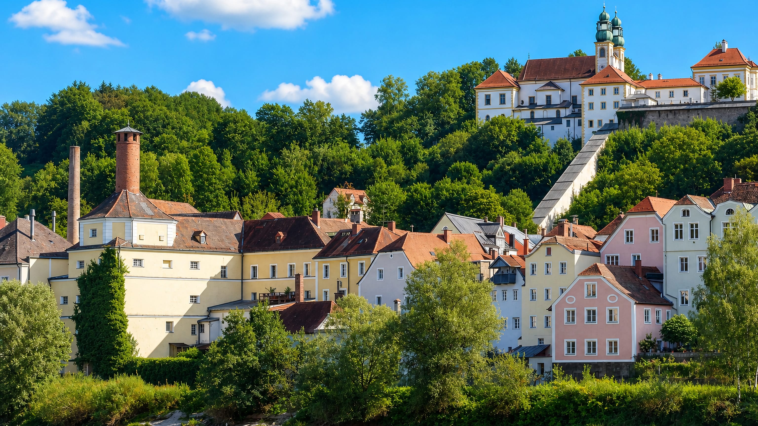 Pastel houses along the Inn in Passau's Innstadt below the twin-domed Mariahilf pilgrimage church.