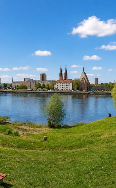 Frankfurt (Oder) riverfront across the Oder river, with twin church spires over the town and a grassy park in front