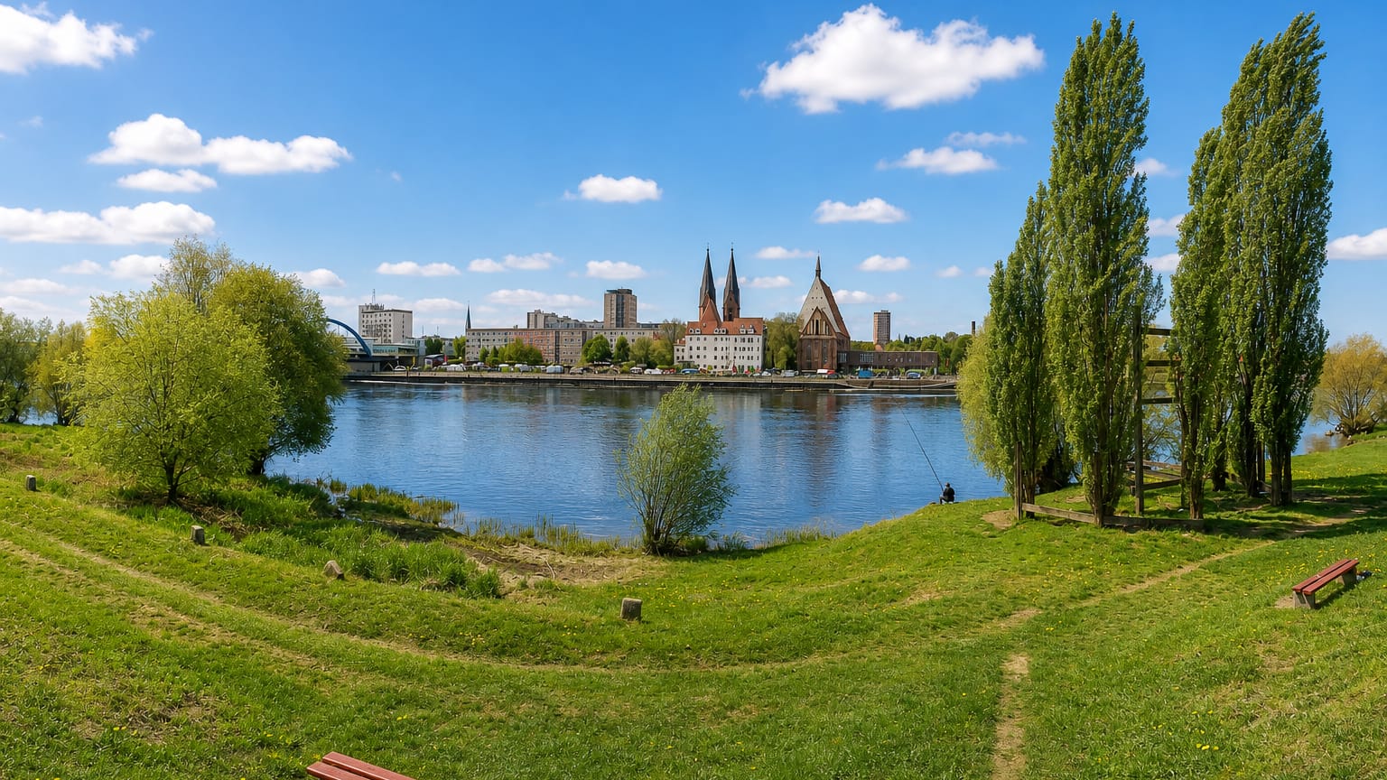 Frankfurt (Oder) riverfront across the Oder river, with twin church spires over the town and a grassy park in front