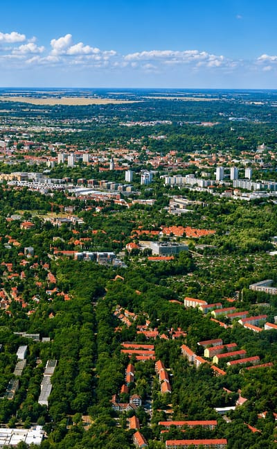 Aerial daytime panorama of Potsdam, red-roofed districts and tower blocks amid greenery beside the Havel lakes.