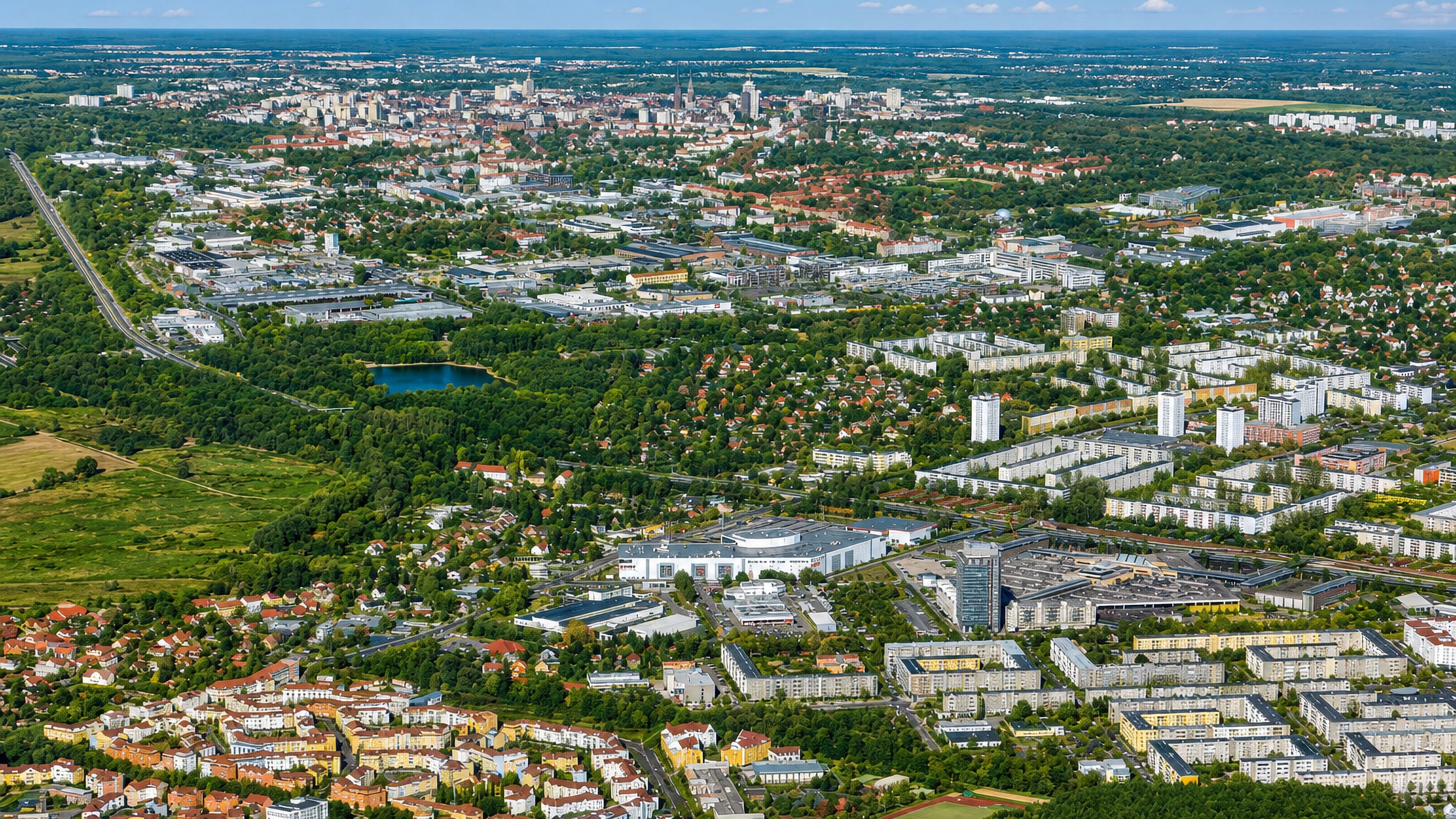 Aerial view over Drewitz in Potsdam, with prefab housing blocks, wooded parkland and the city skyline beyond.
