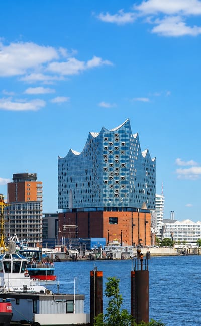 Hamburg waterfront in Altona with the wave-roofed Elbphilharmonie concert hall rising over the Elbe river and harbour boats.