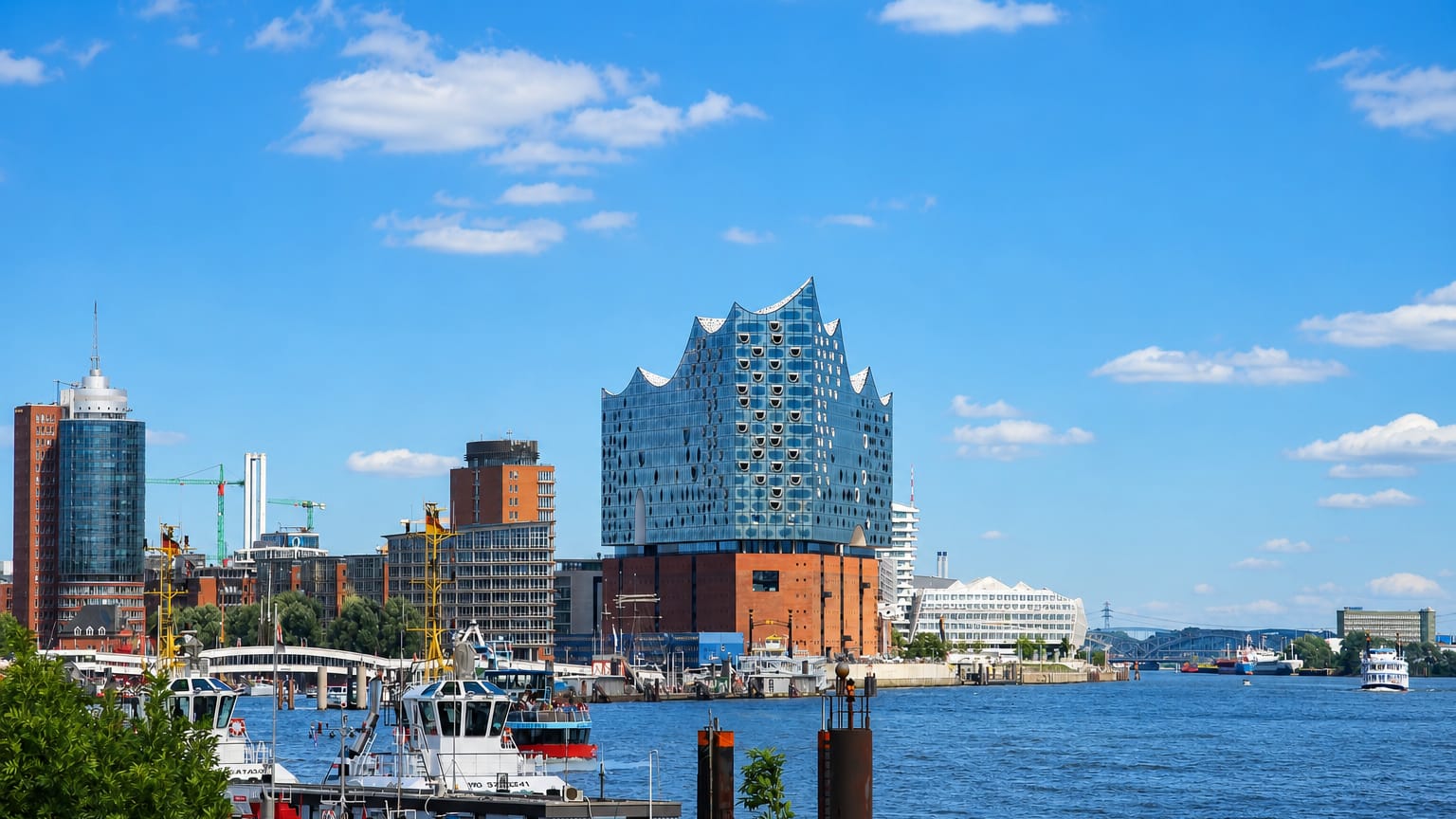 Hamburg waterfront in Altona with the wave-roofed Elbphilharmonie concert hall rising over the Elbe river and harbour boats.