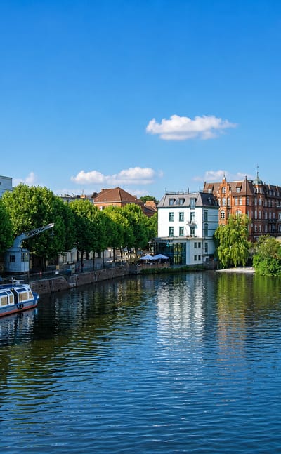 A moored tour boat on a calm tree-lined canal beside townhouses in Bergedorf, Hamburg.