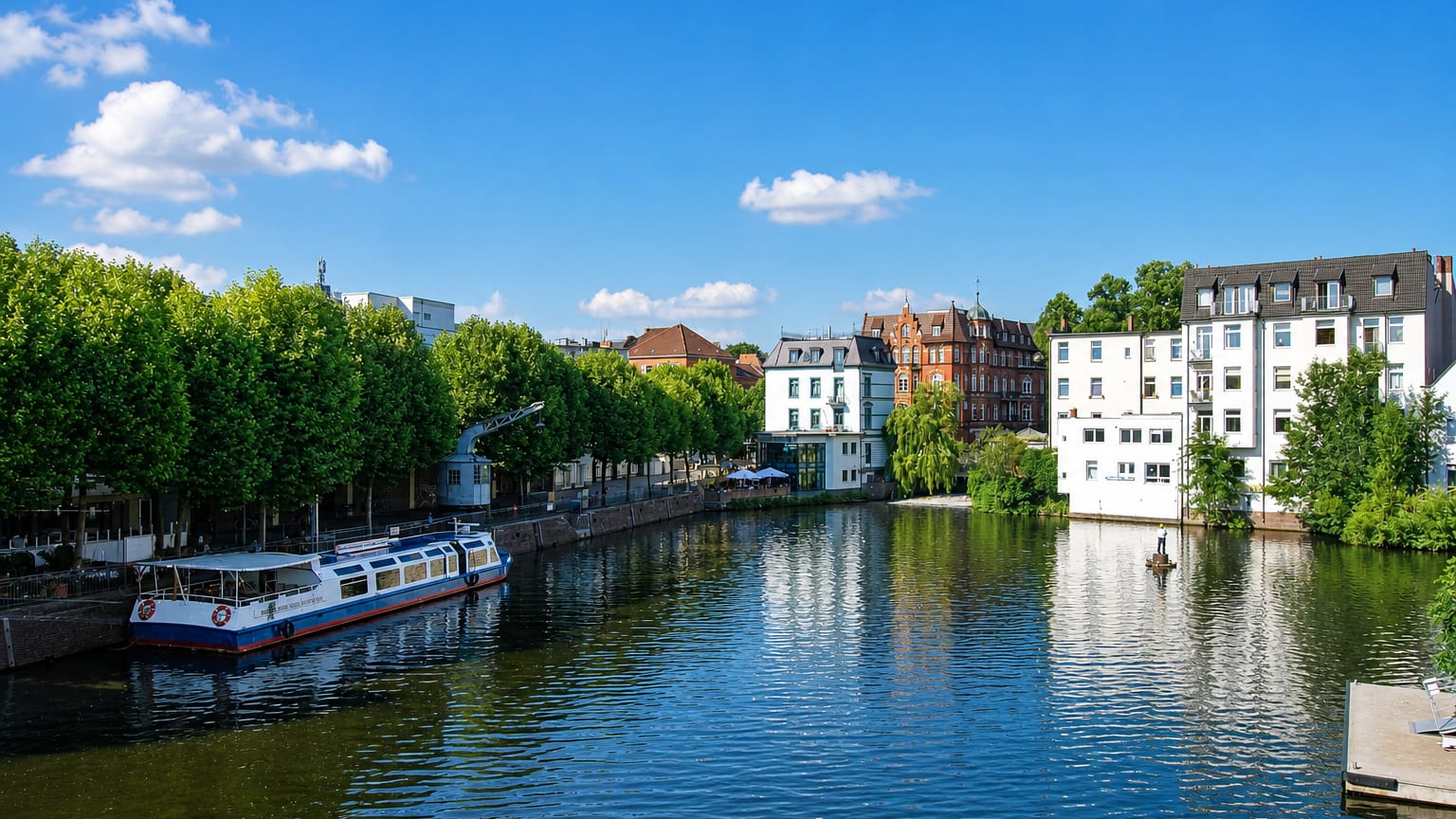 A moored tour boat on a calm tree-lined canal beside townhouses in Bergedorf, Hamburg.