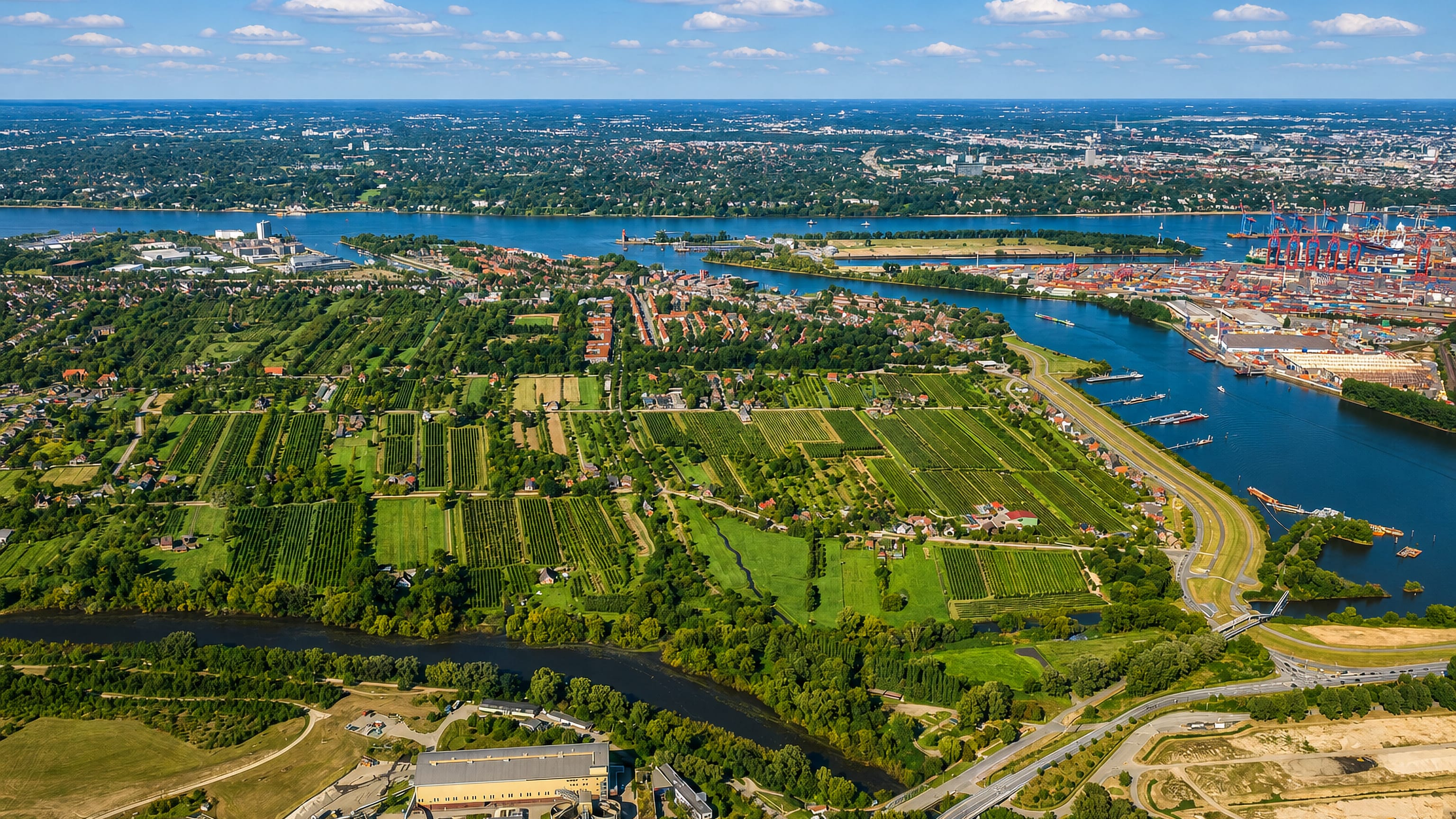 Aerial view of Finkenwerder's green orchards and fields on the Elbe, with Hamburg's container port terminal beyond.