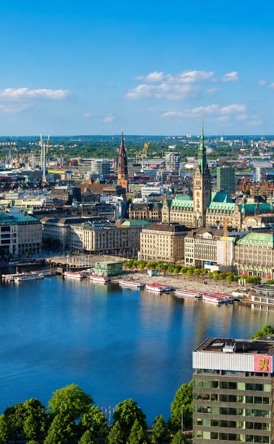Hamburg-Mitte skyline over the Alster lake with the city hall and historic church spires under a blue sky.
