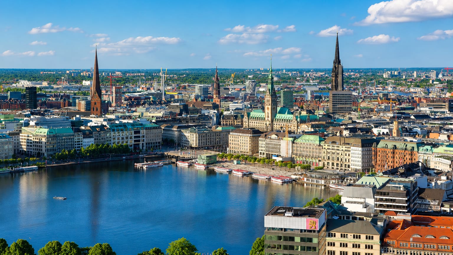 Hamburg-Mitte skyline over the Alster lake with the city hall and historic church spires under a blue sky.
