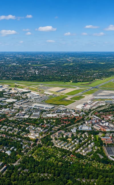 High aerial of Hamburg-Nord showing Hamburg Airport runways amid leafy residential neighbourhoods under a blue sky.