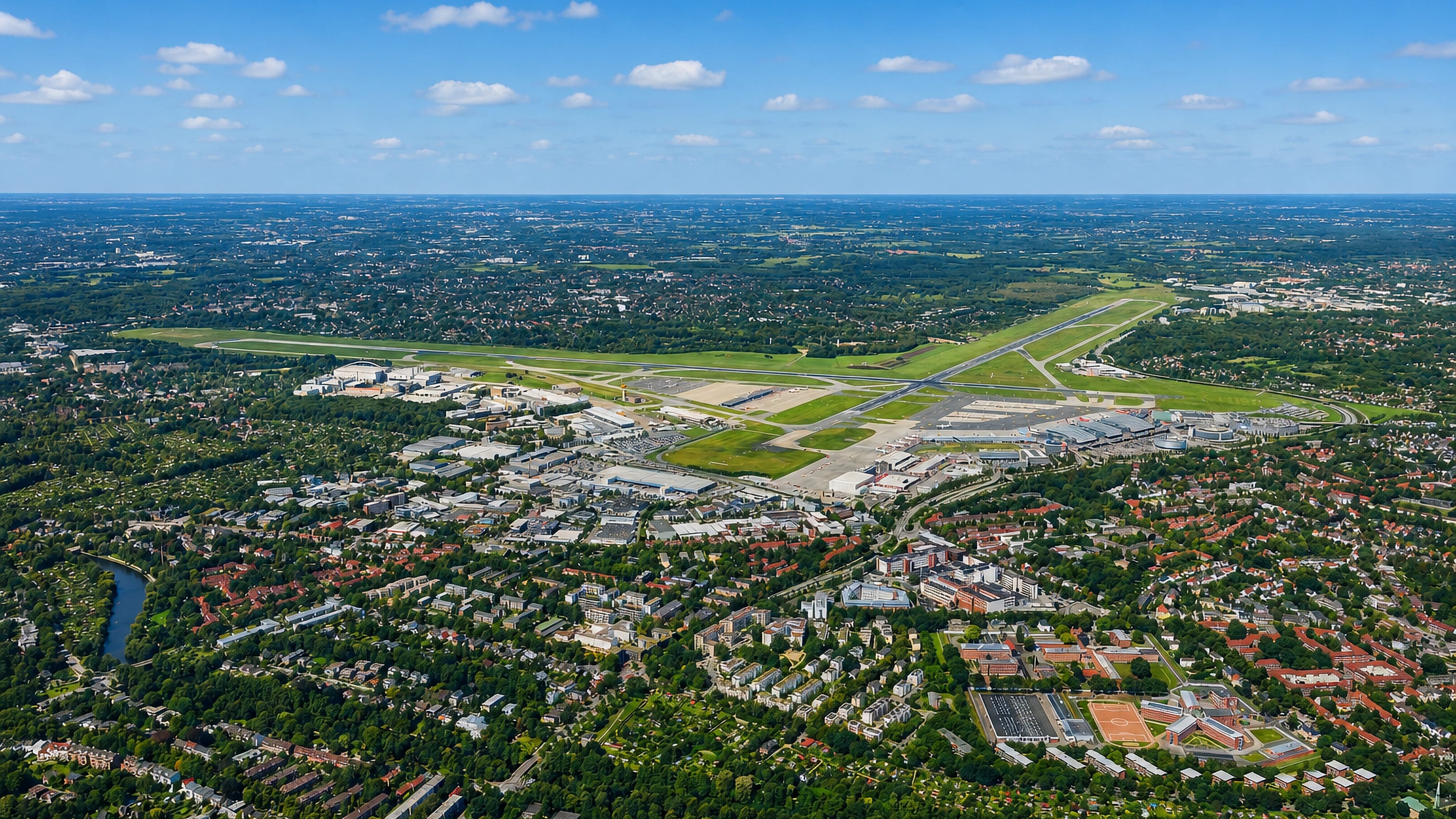 High aerial of Hamburg-Nord showing Hamburg Airport runways amid leafy residential neighbourhoods under a blue sky.