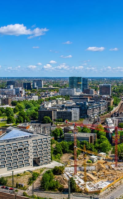 Aerial view over the Hammerbrook district of Hamburg with mid-rise offices, rail lines and construction cranes under blue sky.