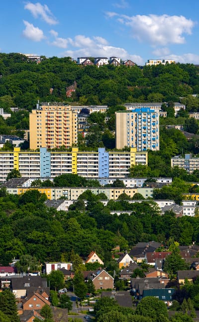 Yellow and blue high-rise apartment estates on a wooded hillside above detached houses in Hausbruch, Hamburg