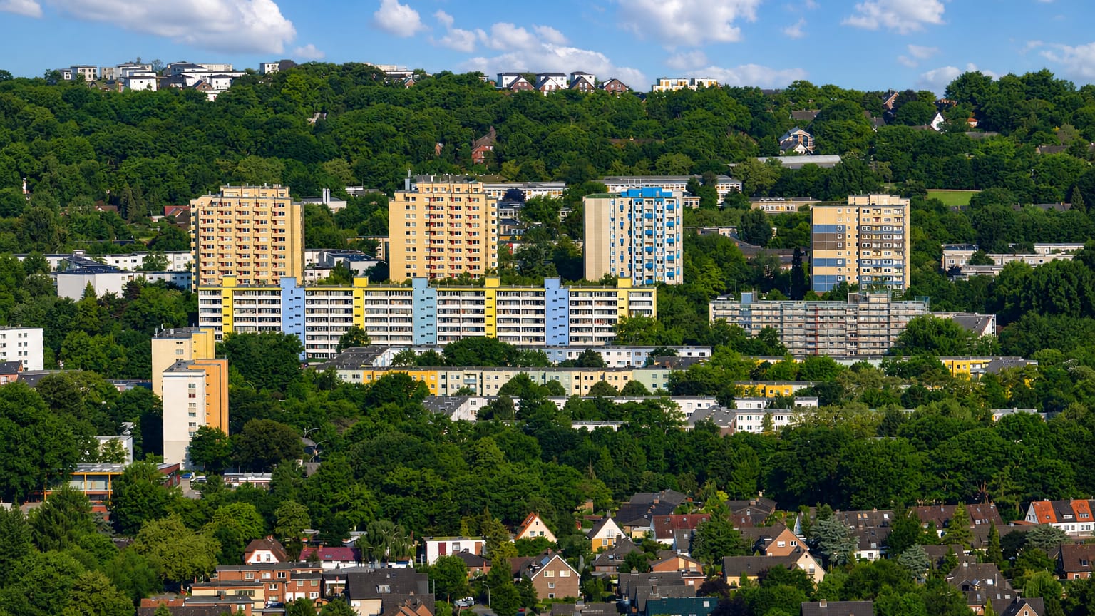 Yellow and blue high-rise apartment estates on a wooded hillside above detached houses in Hausbruch, Hamburg