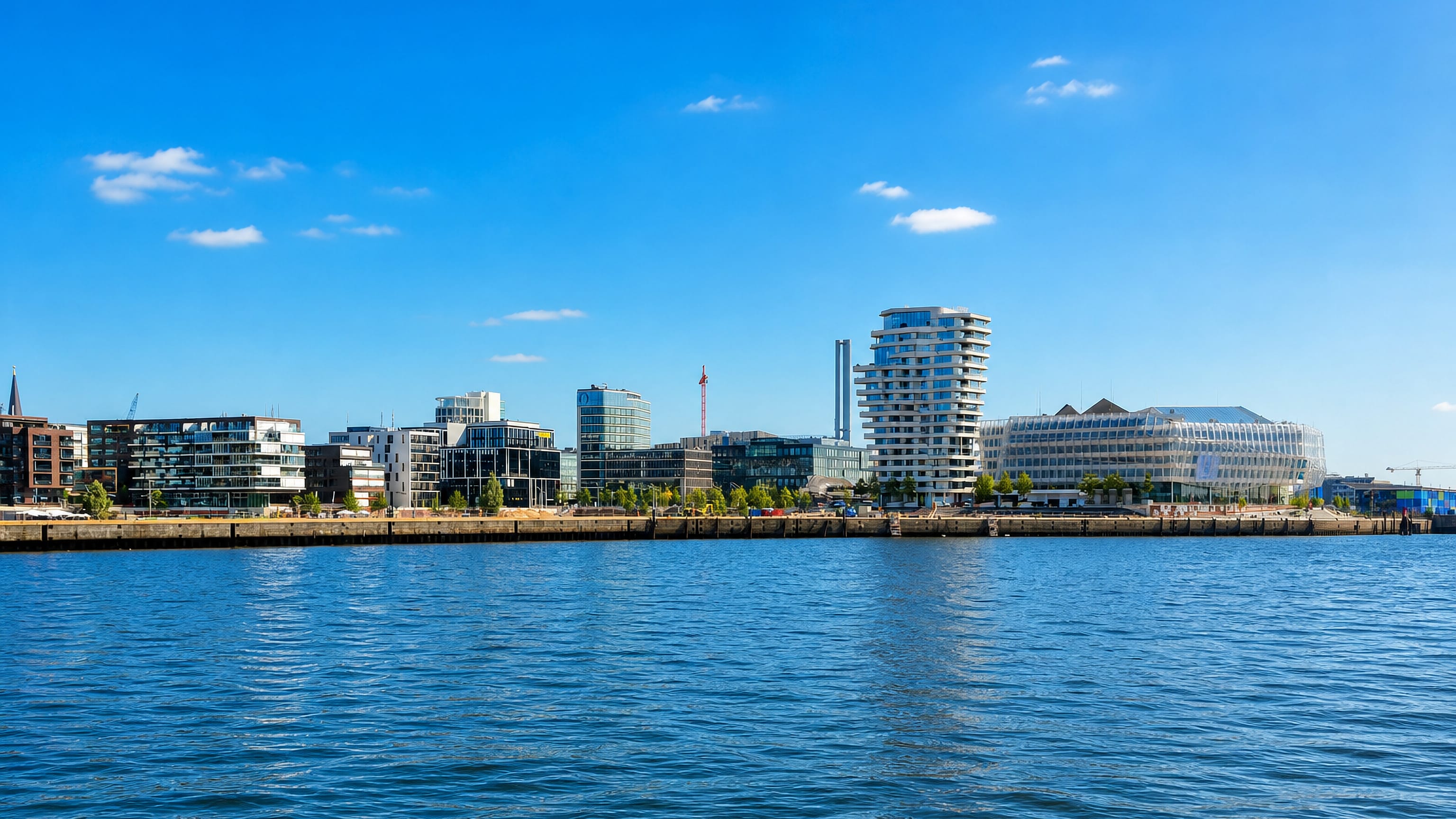 Hamburg's HafenCity waterfront on the Elbe, with the wave-topped Marco Polo Tower and modern quayside buildings.