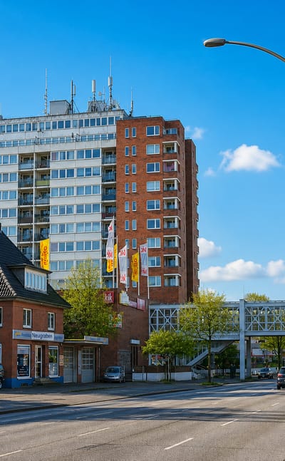 Street scene in Neugraben-Fischbek, Hamburg, with a brick high-rise tower marked Neugraben, a pedestrian bridge and passing traffic.
