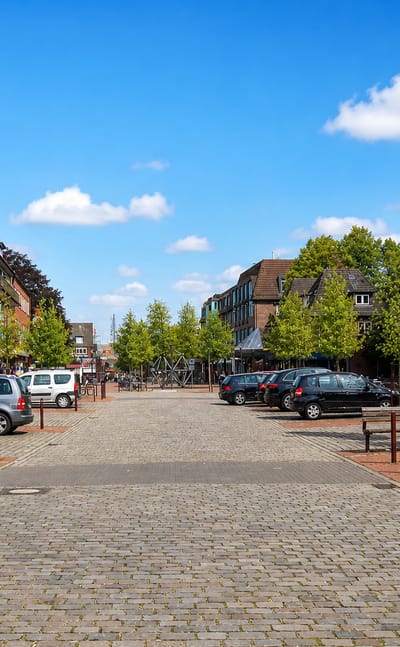 Pedestrianised market square in Niendorf, Hamburg, lined with brick shop buildings, trees and cobblestone paving.
