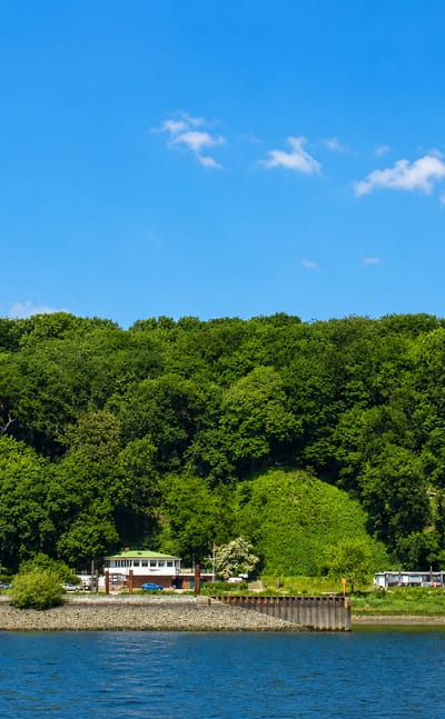 The wooded Elbe riverbank at Nienstedten in Hamburg with villas along the shore and a red-and-white striped lighthouse.