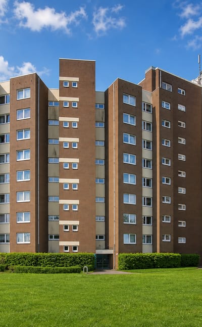 Brown-brick 1970s high-rise apartment towers on a green lawn under a blue sky in Steilshoop, Hamburg