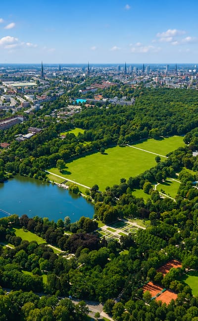 Aerial view over a large green city park with a lake and boating pond, with Hamburg's Winterhude and its skyline beyond