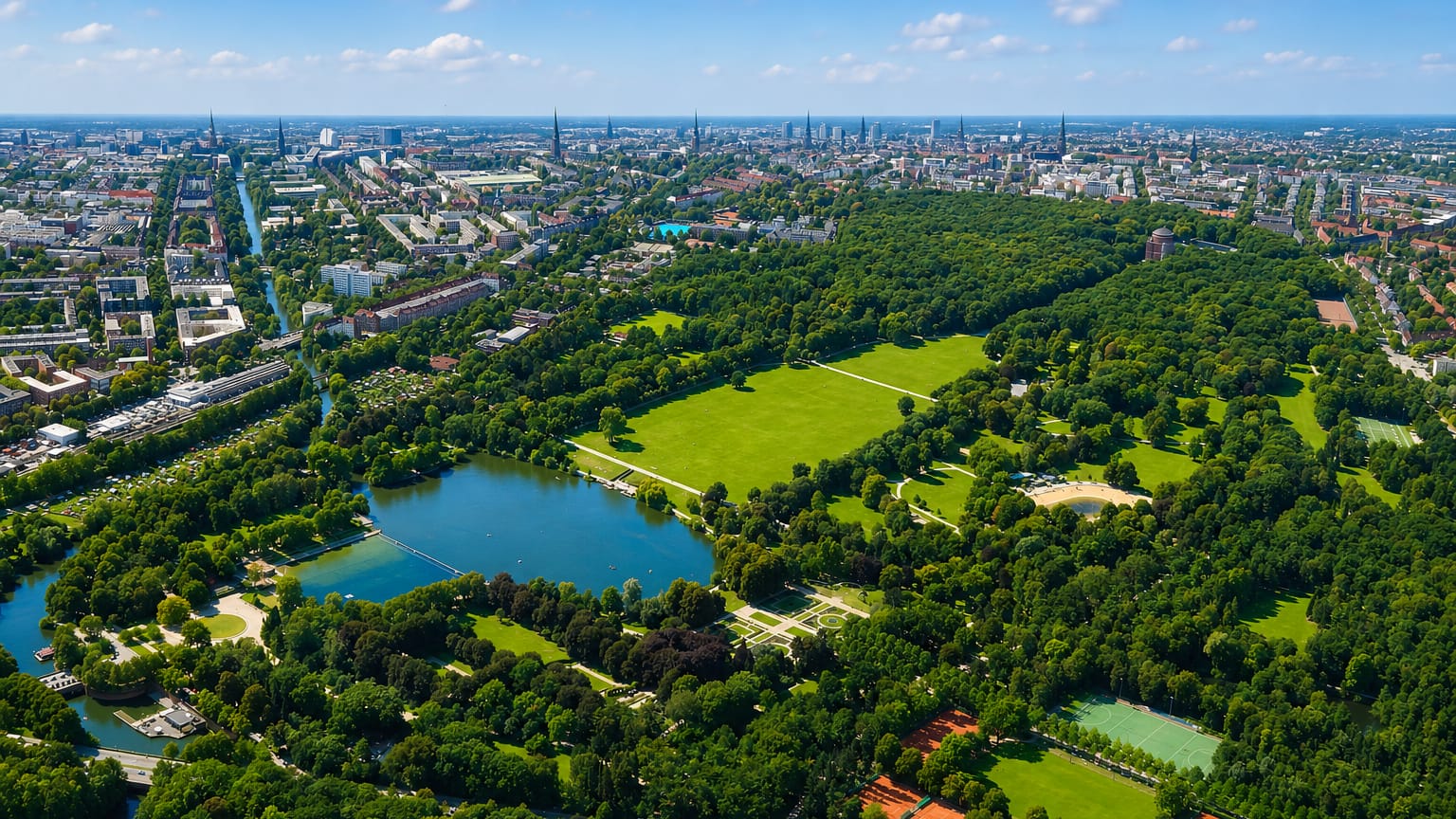 Aerial view over a large green city park with a lake and boating pond, with Hamburg's Winterhude and its skyline beyond