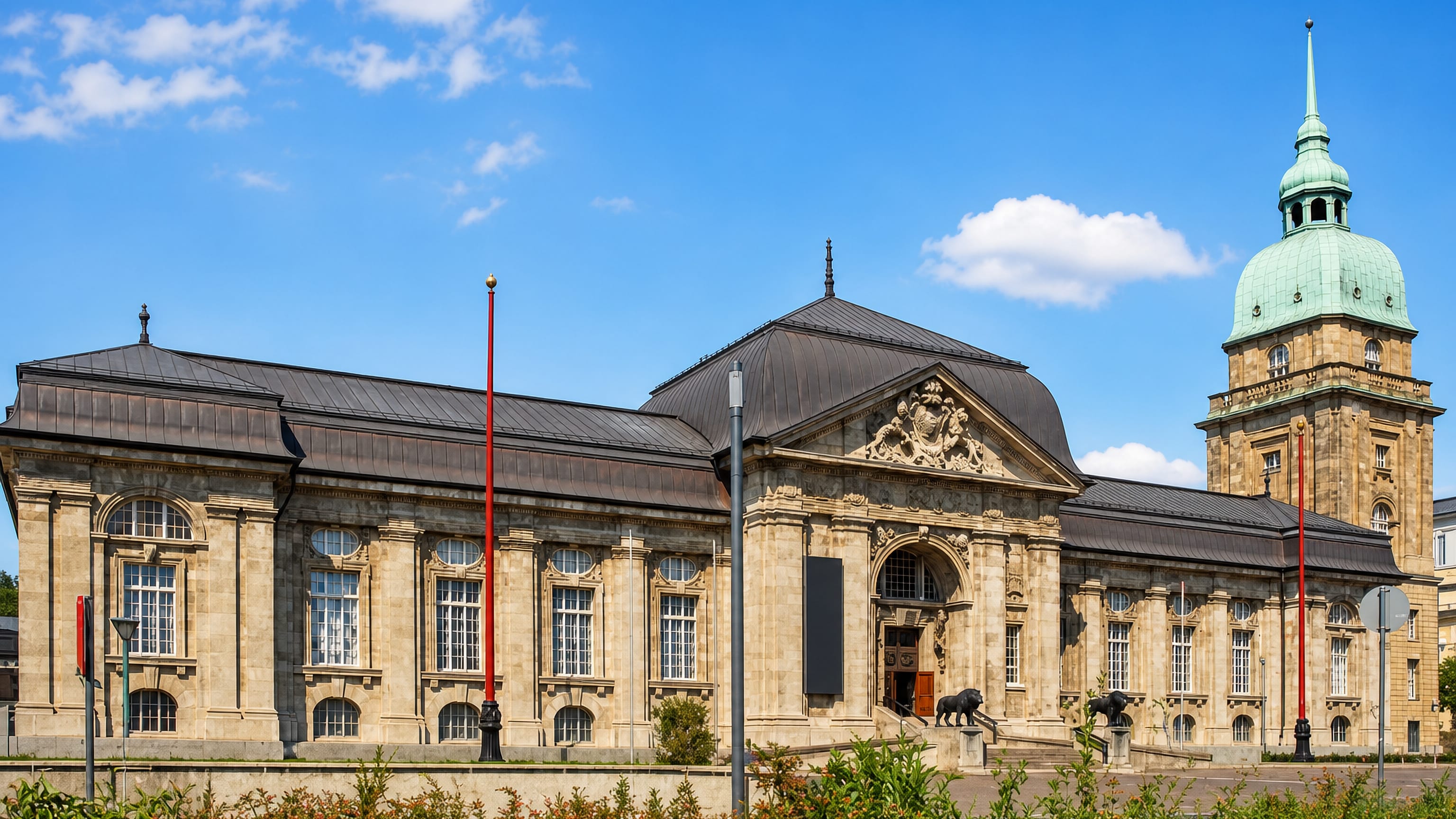 The Hessisches Landesmuseum Darmstadt, its green copper dome tower and bronze lions bright under a blue summer sky.