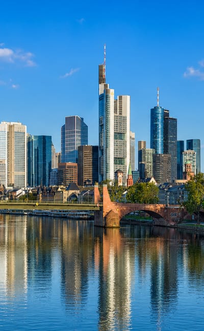 Frankfurt's high-rise financial skyline and red cathedral reflected in the river Main, seen past the Alte Brücke.