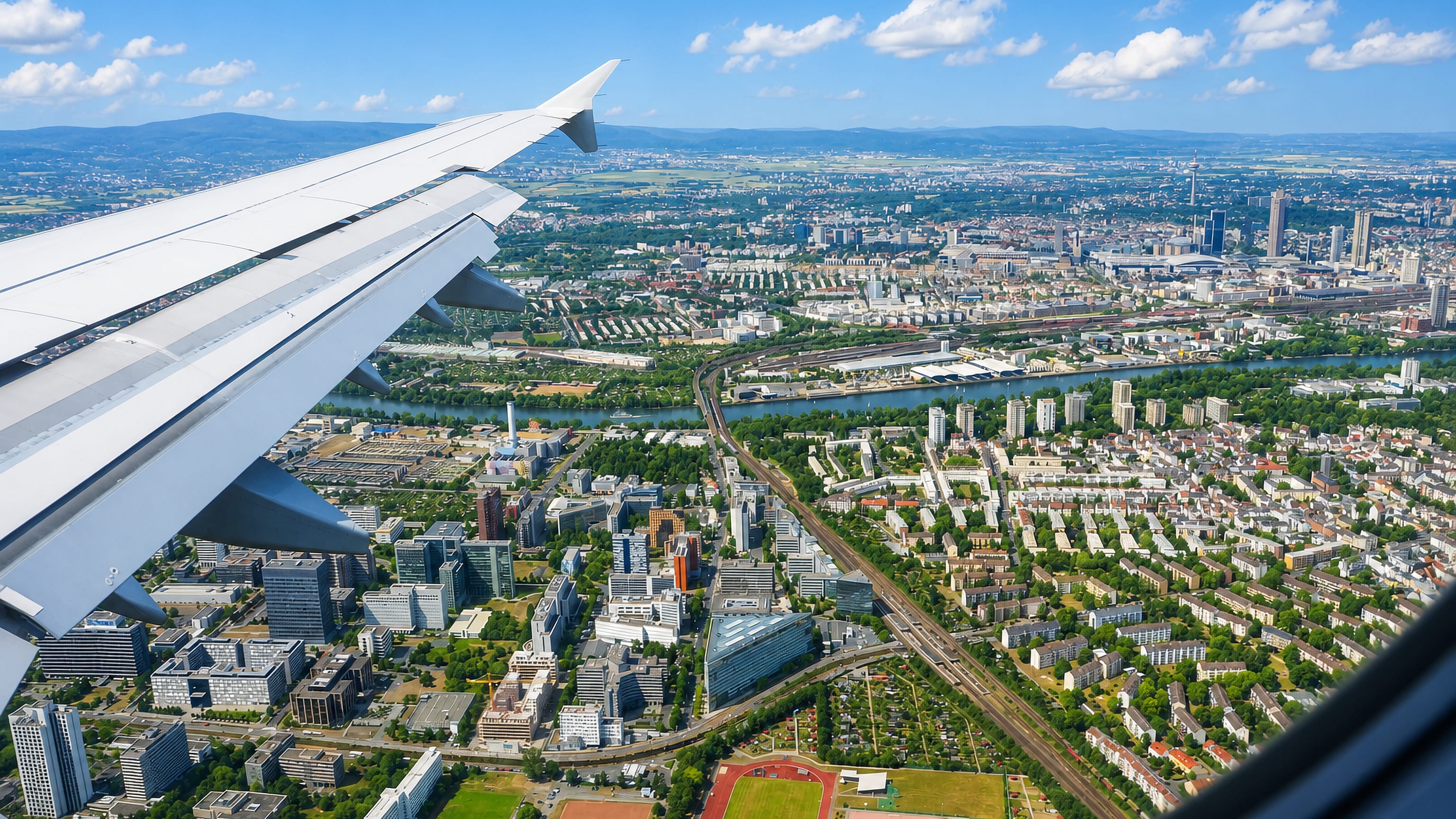 Aerial view over Niederrad's office towers and the river Main toward the Frankfurt skyline, seen past an aircraft wing