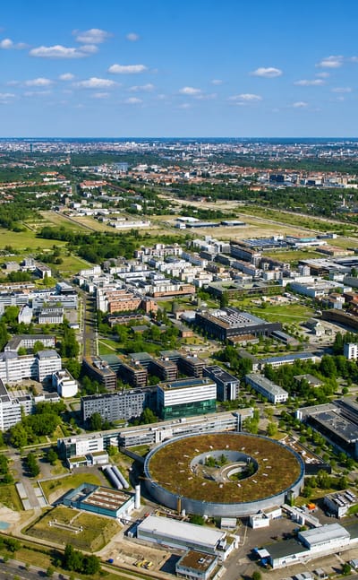 Aerial view of the Adlershof science and technology park with its circular electron-storage-ring building and the Berlin skyline beyond