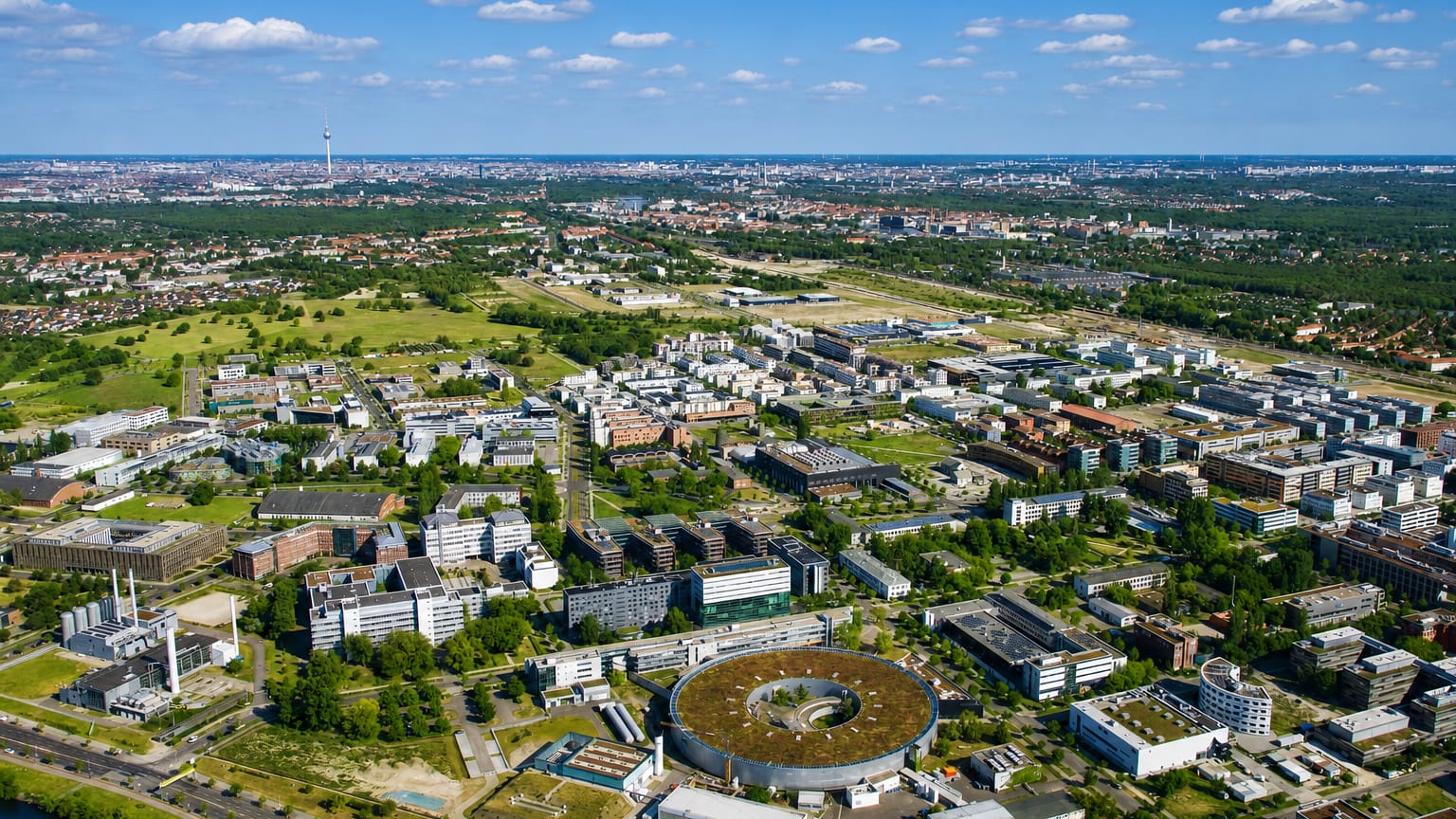 Aerial view of the Adlershof science and technology park with its circular electron-storage-ring building and the Berlin skyline beyond