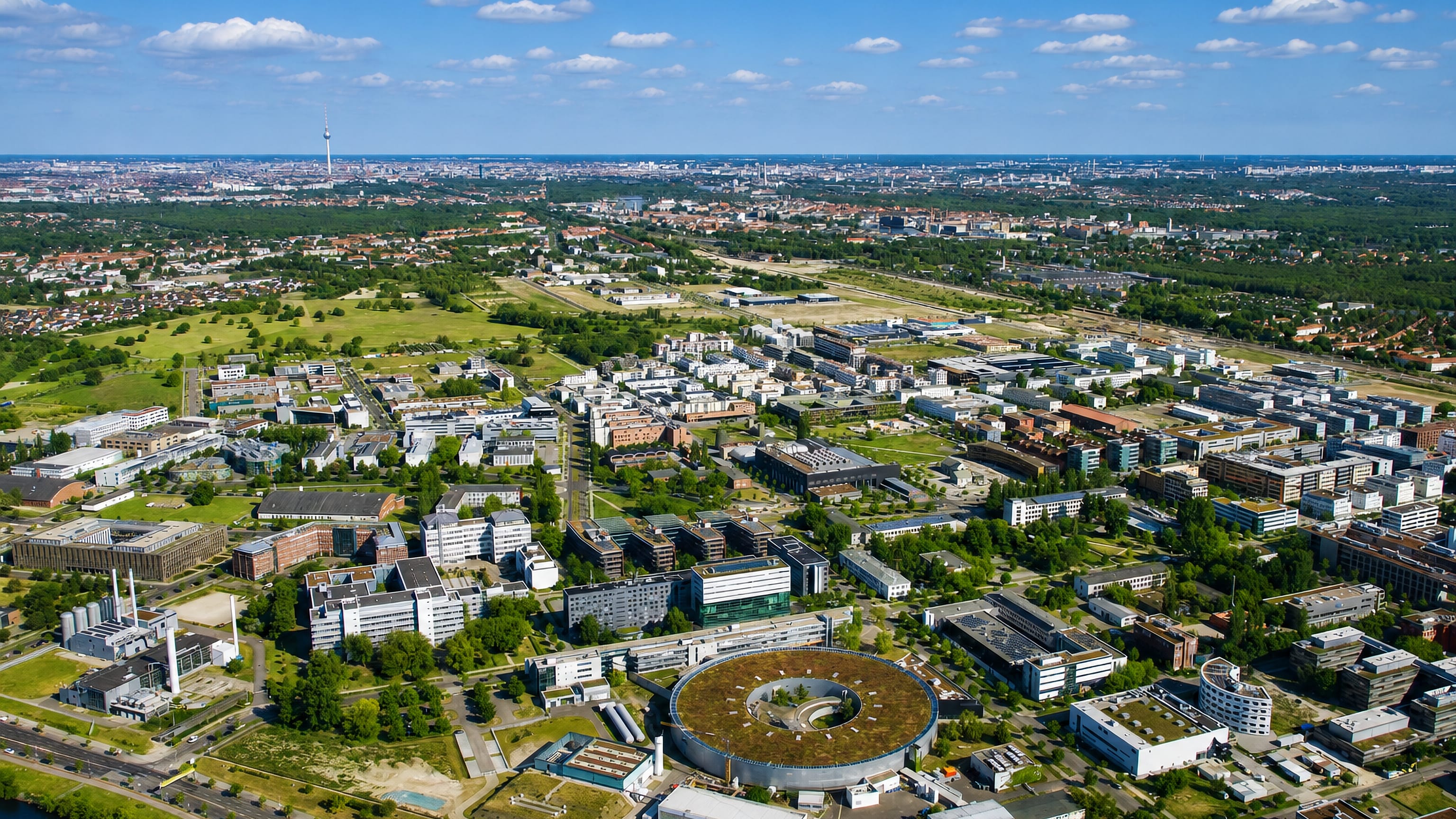 Aerial view of the Adlershof science and technology park with its circular electron-storage-ring building and the Berlin skyline beyond