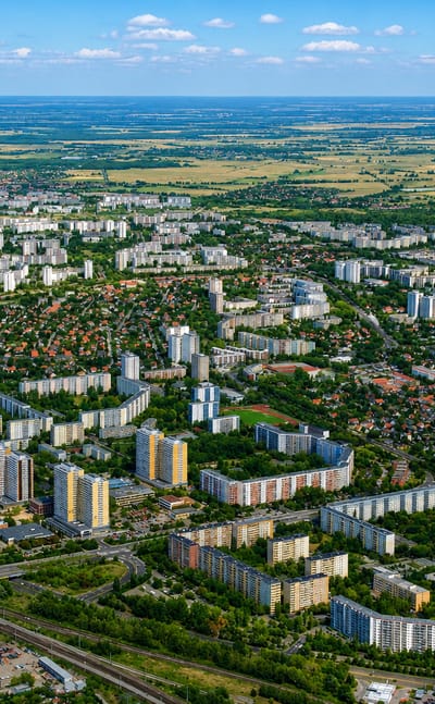Aerial view of Biesdorf's prefab housing blocks, rail lines and greenery on Berlin's eastern edge under a blue sky