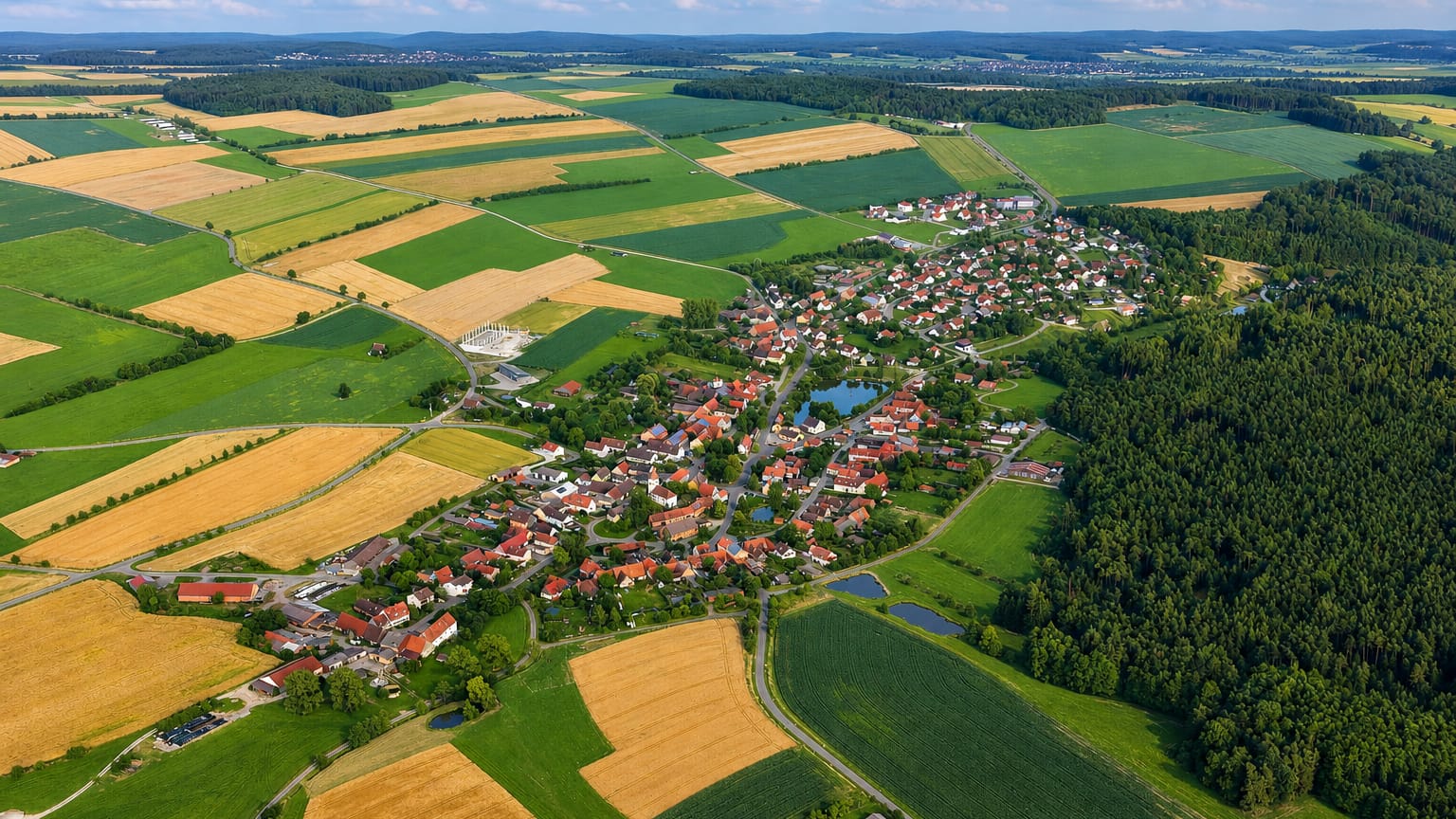 Aerial of a small village ringed by patchwork farm fields and forest near Buch, Berlin