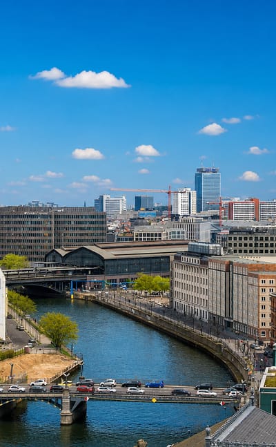 Berlin cityscape along the Spree with the Fernsehturm TV tower and the Berliner Dom cupola under a blue sky.