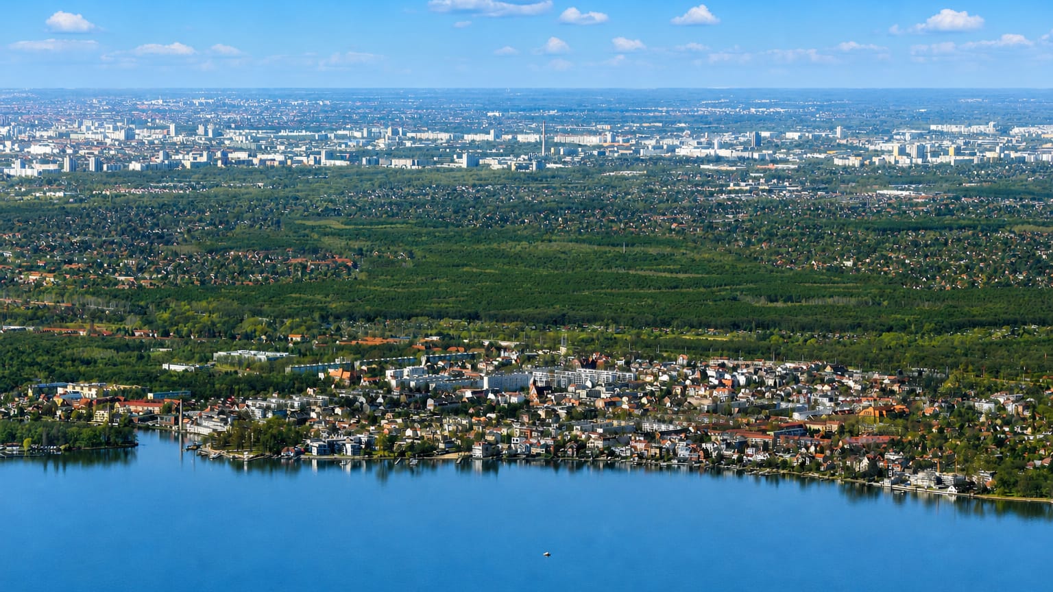 Aerial view of Friedrichshagen on the shore of Berlin's Müggelsee, ringed by forest with the city beyond.