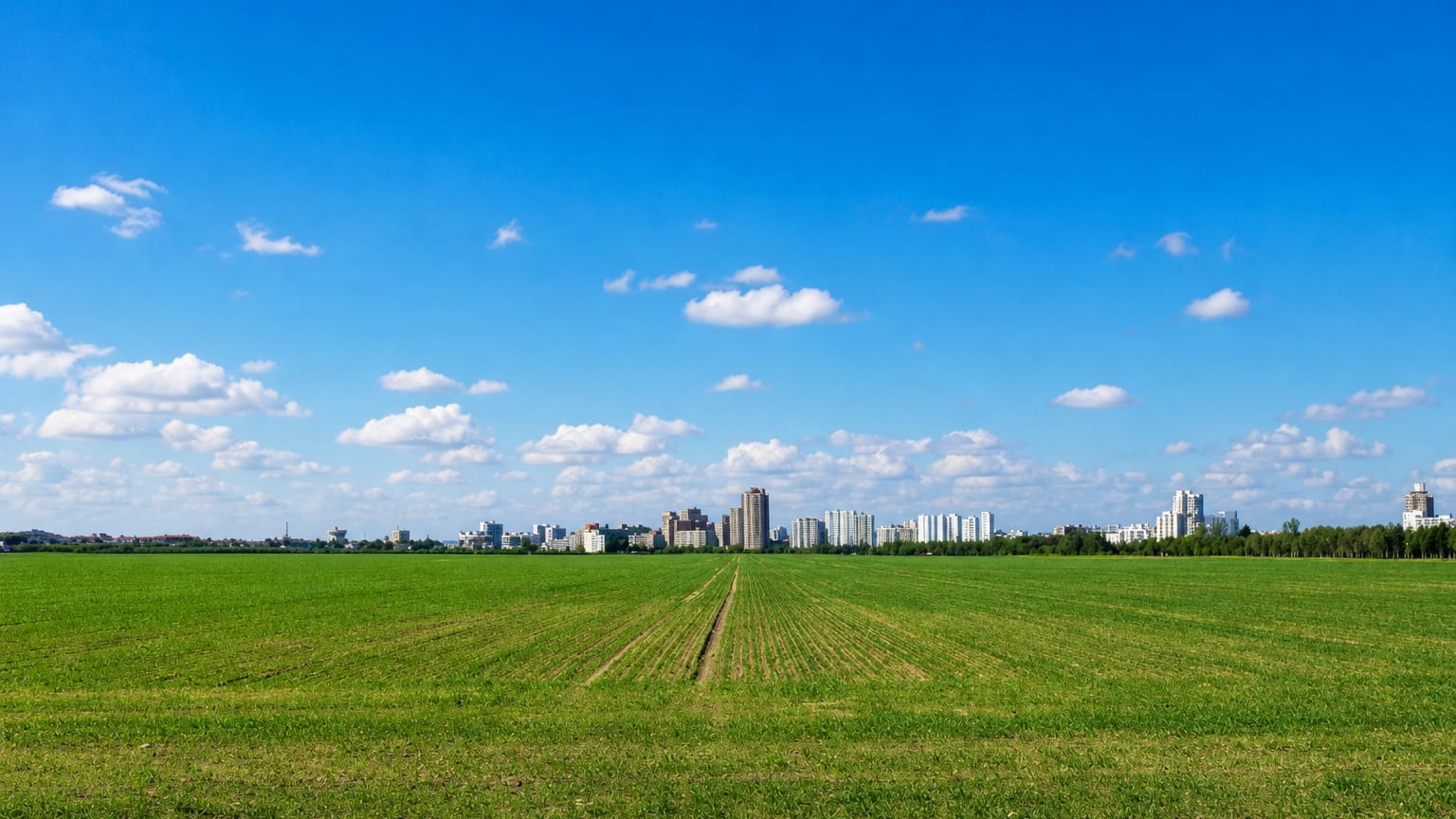 Distant high-rise skyline of the Gropiusstadt estate seen across an open green field in Berlin
