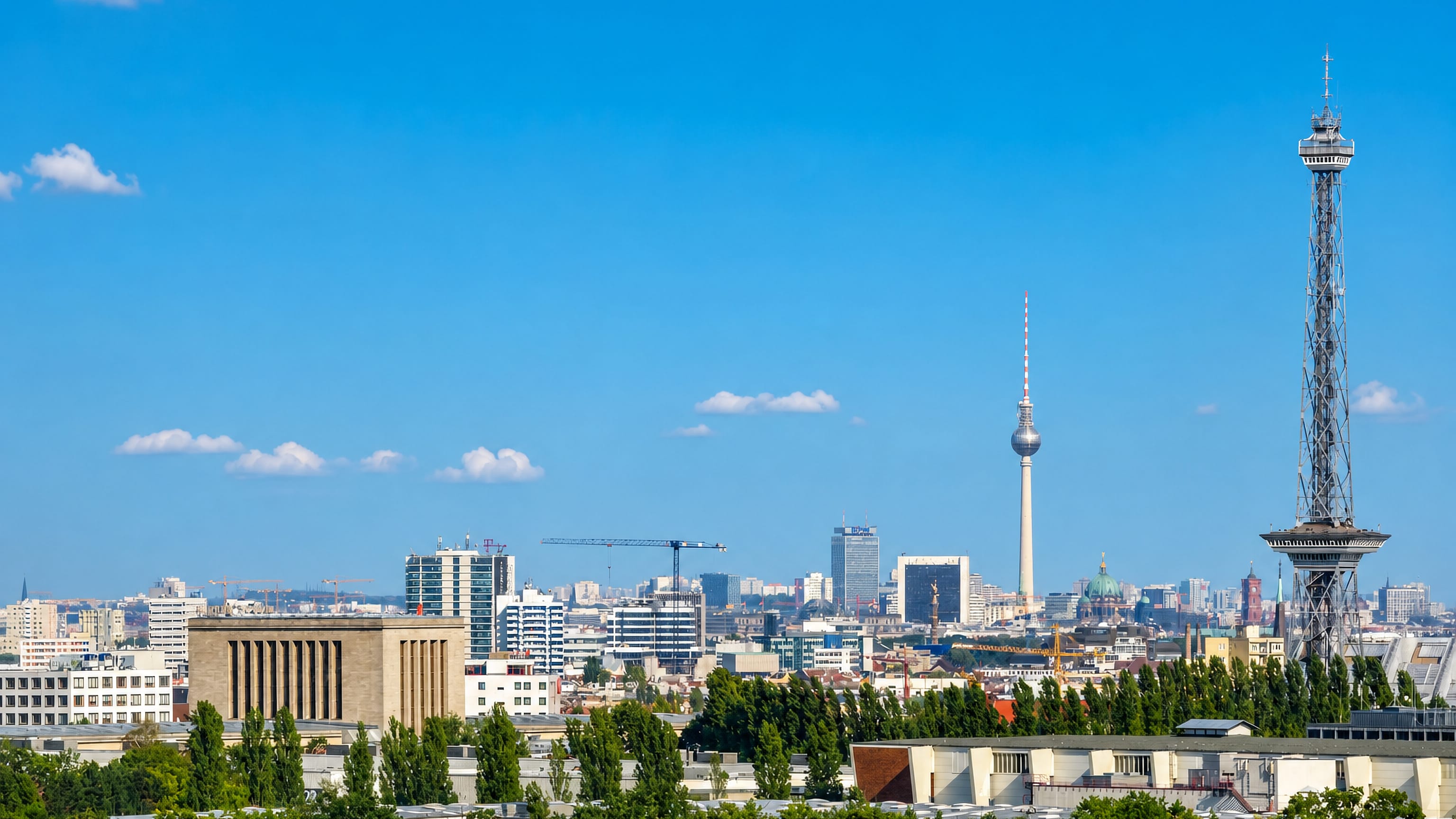 Berlin skyline seen over the treetops of Grunewald, with the Funkturm and the distant TV Tower under a clear sky.