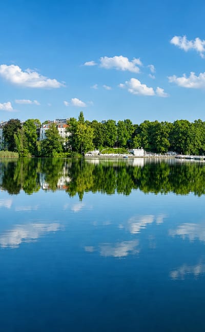 The Halensee lake in Berlin with a tree-lined shore and villas mirrored in calm blue water.